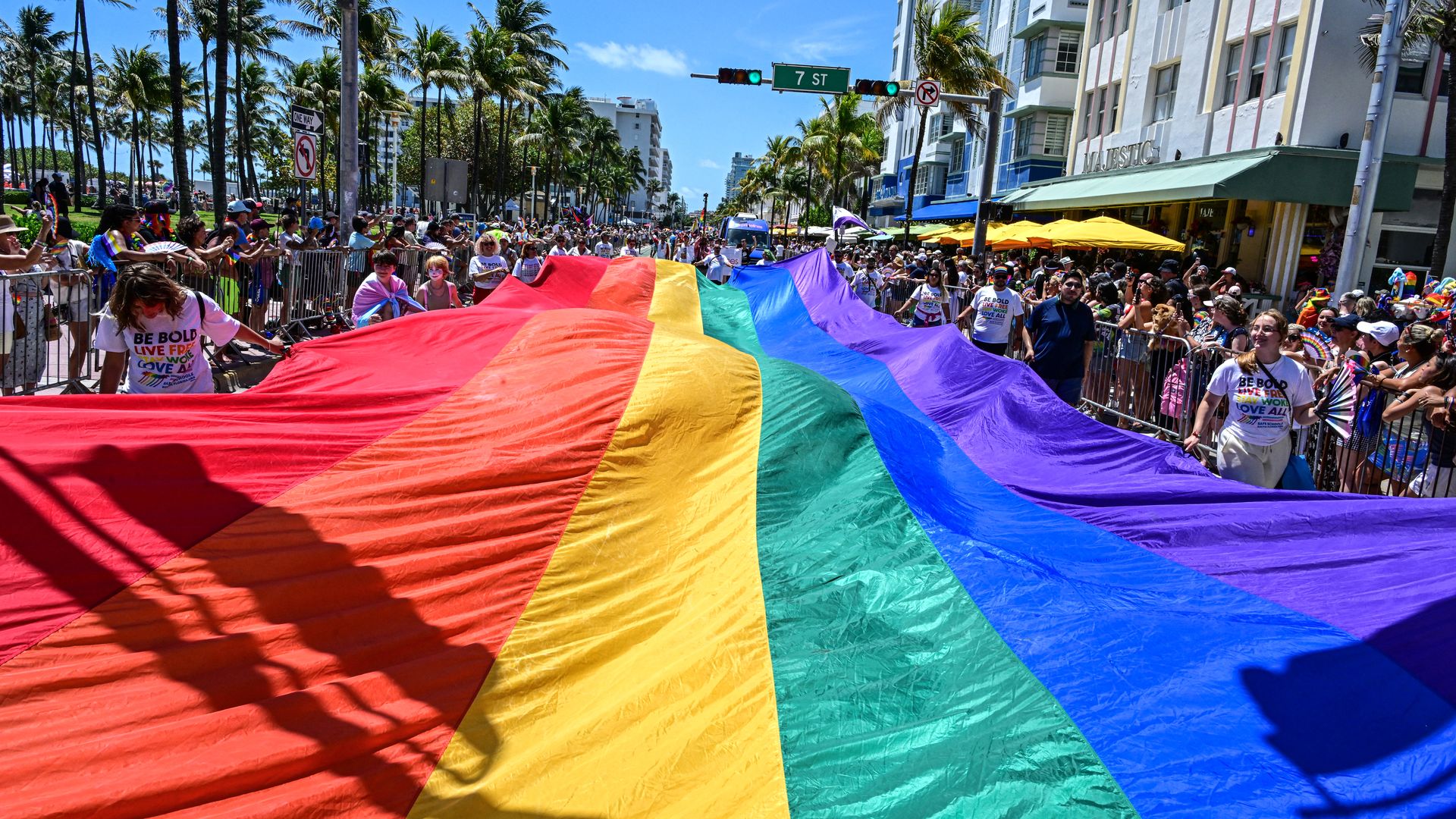 A large rainbow flag in the middle of a parade. 