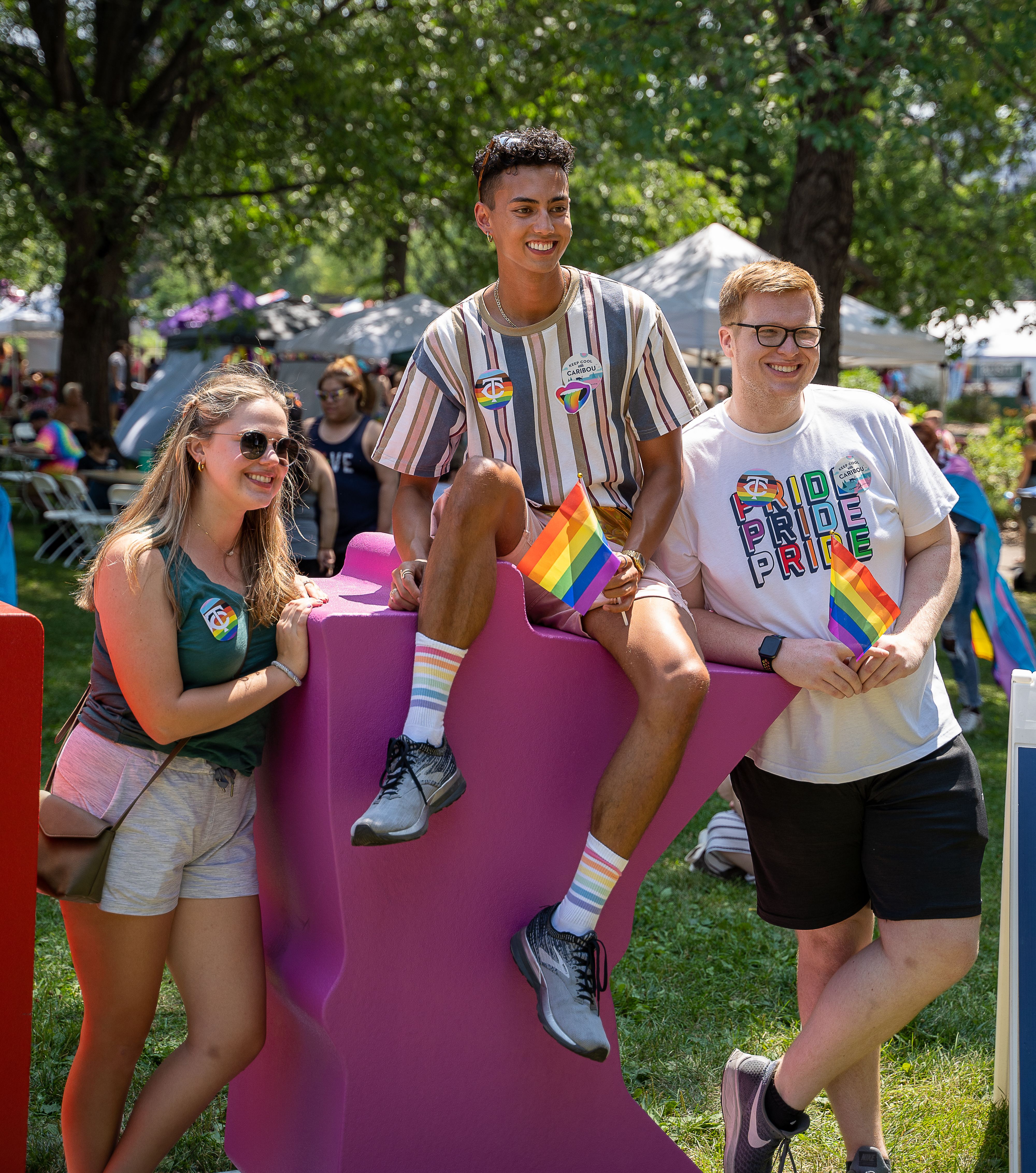 Three people posing for a photo with rainbow flags at a pride event