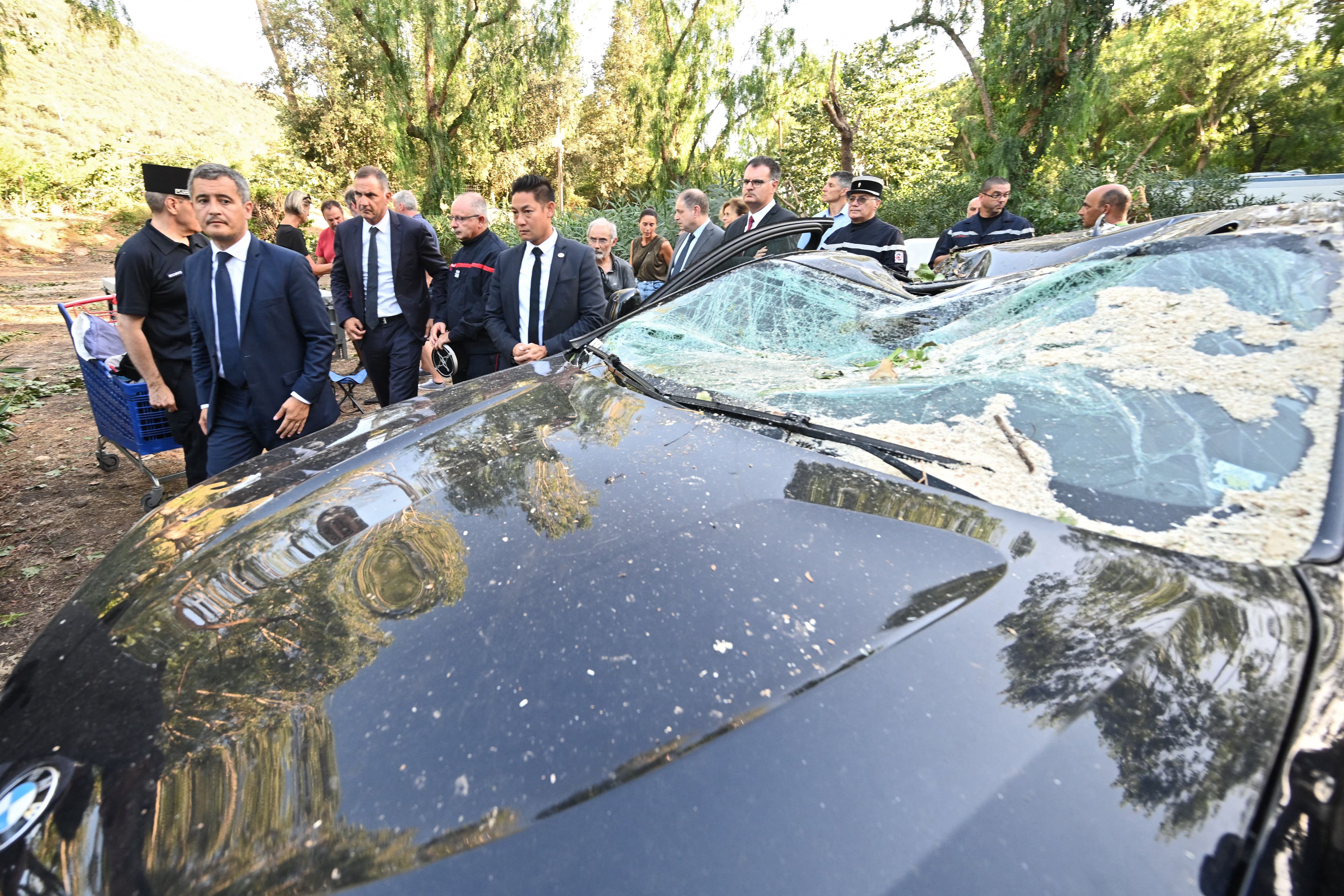 France's Interior Minister Gerald Darmanin (L) walks by a damaged car as he visits the Sagone camping site on the French island of Corsica on Aug. 18.