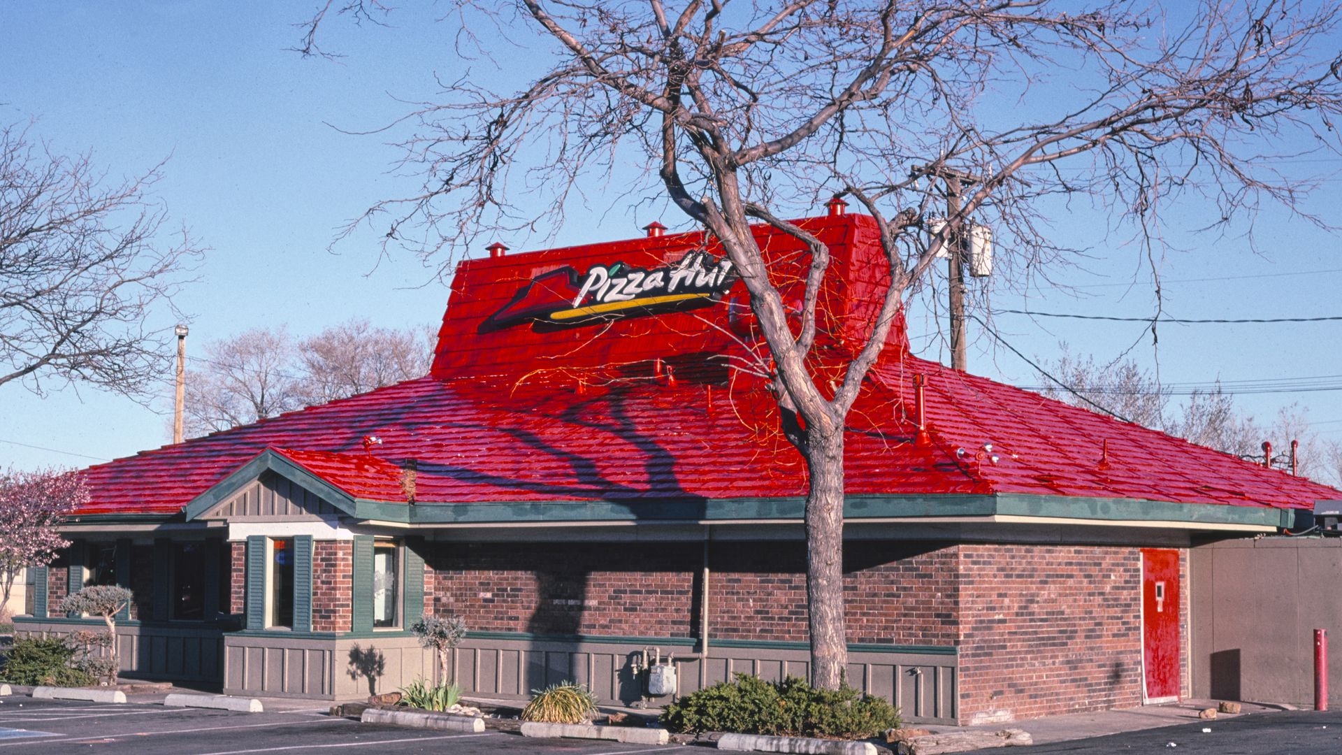 Pizza Hut restaurant with a sloped, four-sided red roof with a steeper, angled top, with a brick exterior below the roof.
