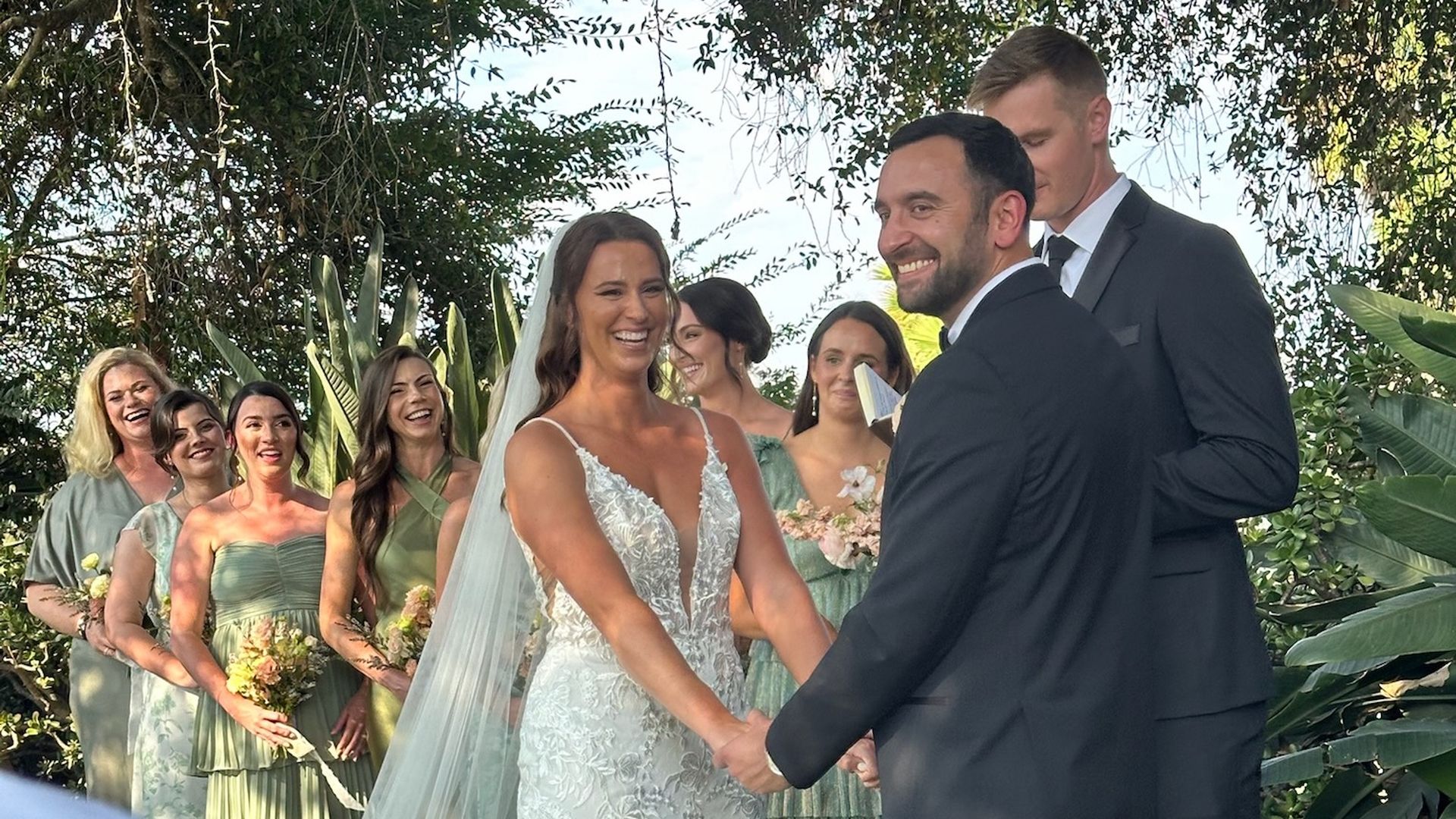Kate laughs while holding her husband's hands at their wedding ceremony.