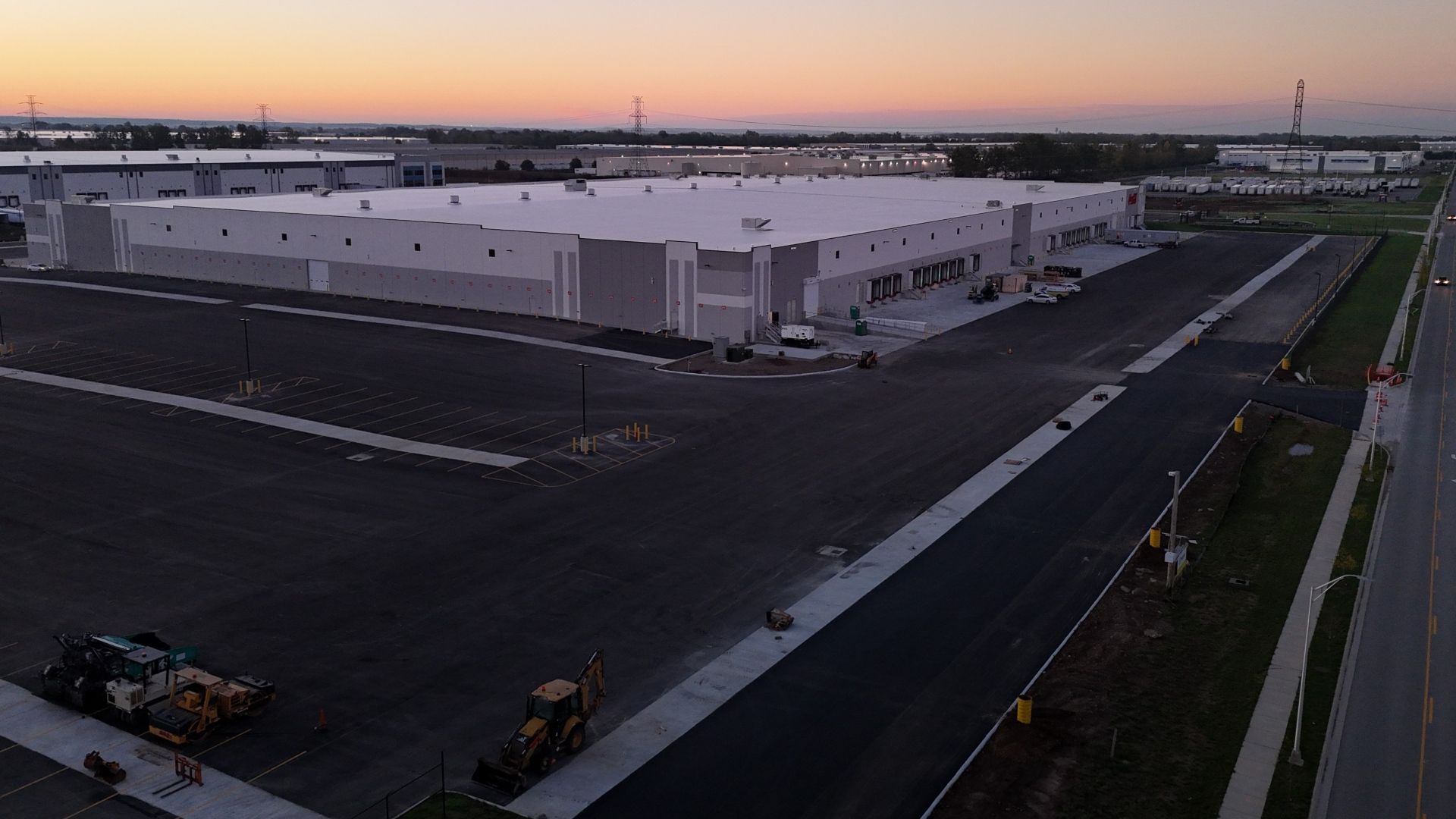 Aerial view of a large industrial warehouse complex at sunrise, showcasing expansive parking areas and loading docks.