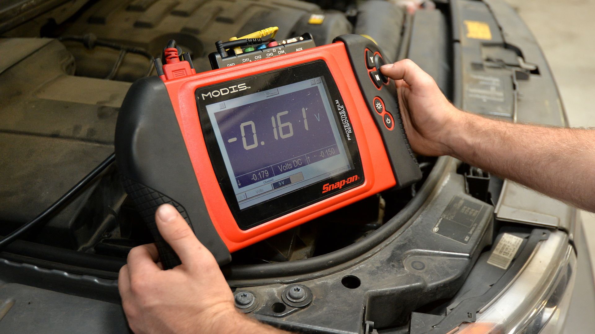 mechanic holds a diagnostic device with display screen over a car's engine block