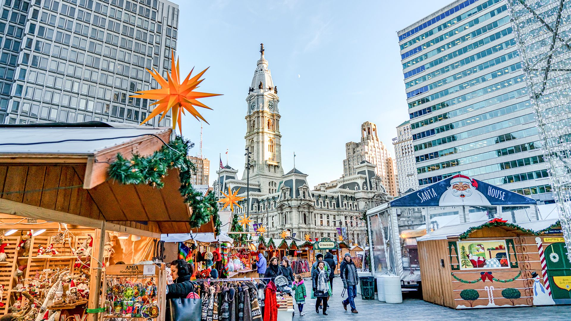 People browse rows of vendors at Christmas Village in Philadelphia with City Hall situated in the background. 