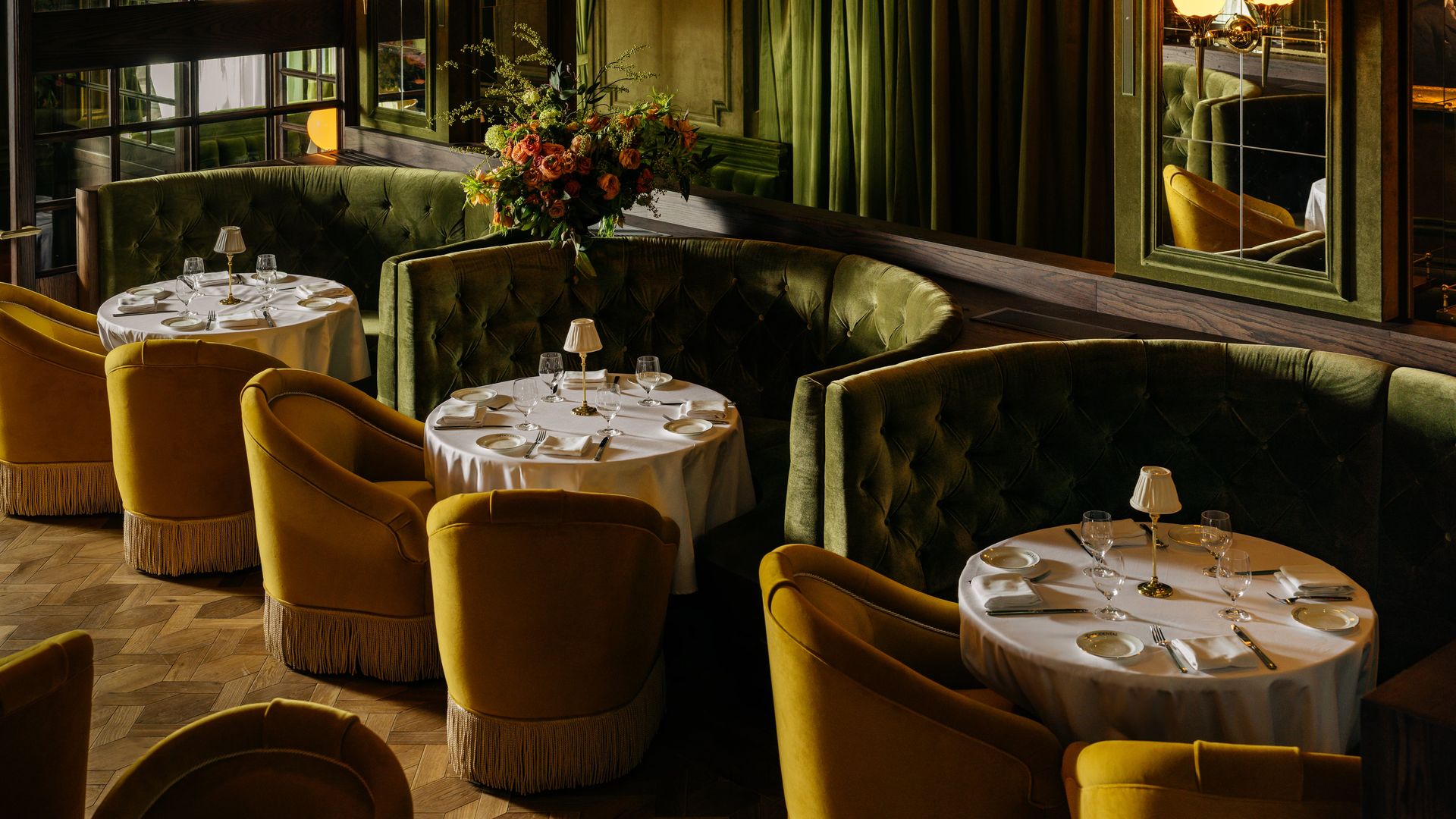 A set of green booths with white tablecloth tables and flowers in an elegant room