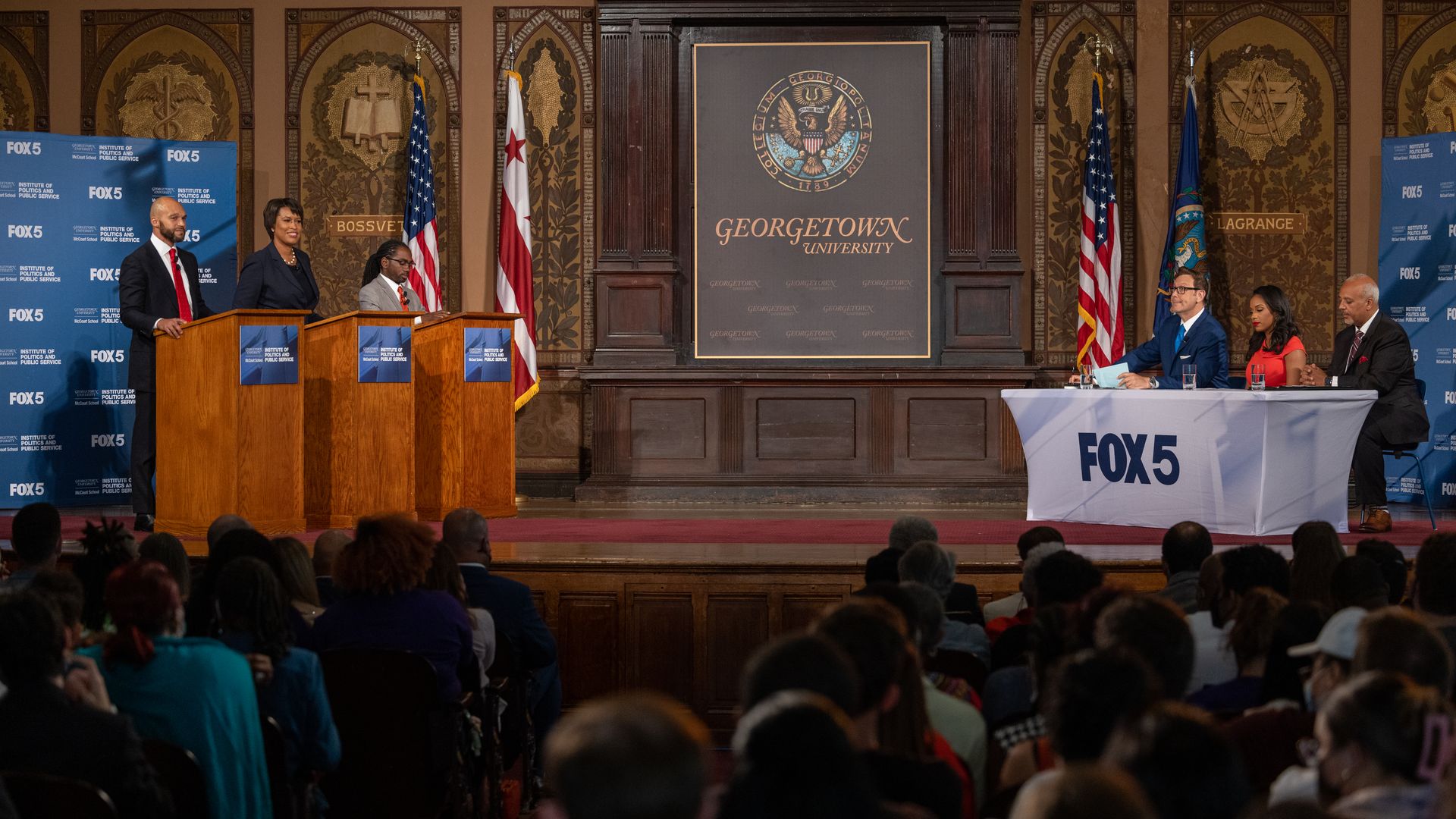 The candidates on stage at podiums with audience in foreground