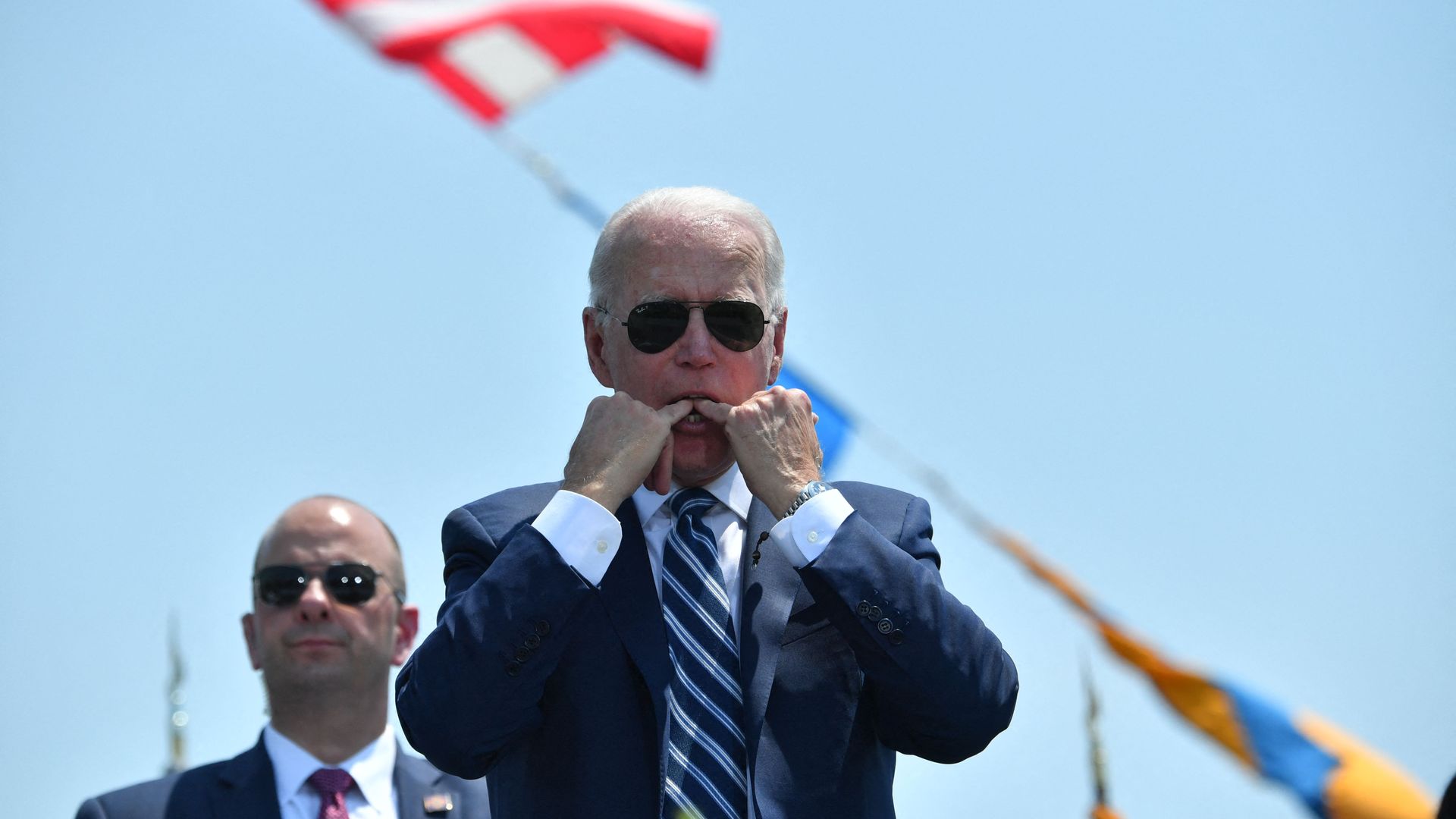 President Biden is seen with fingers in his mouth as he whistles during the Coast Guard Academy graduation ceremony.