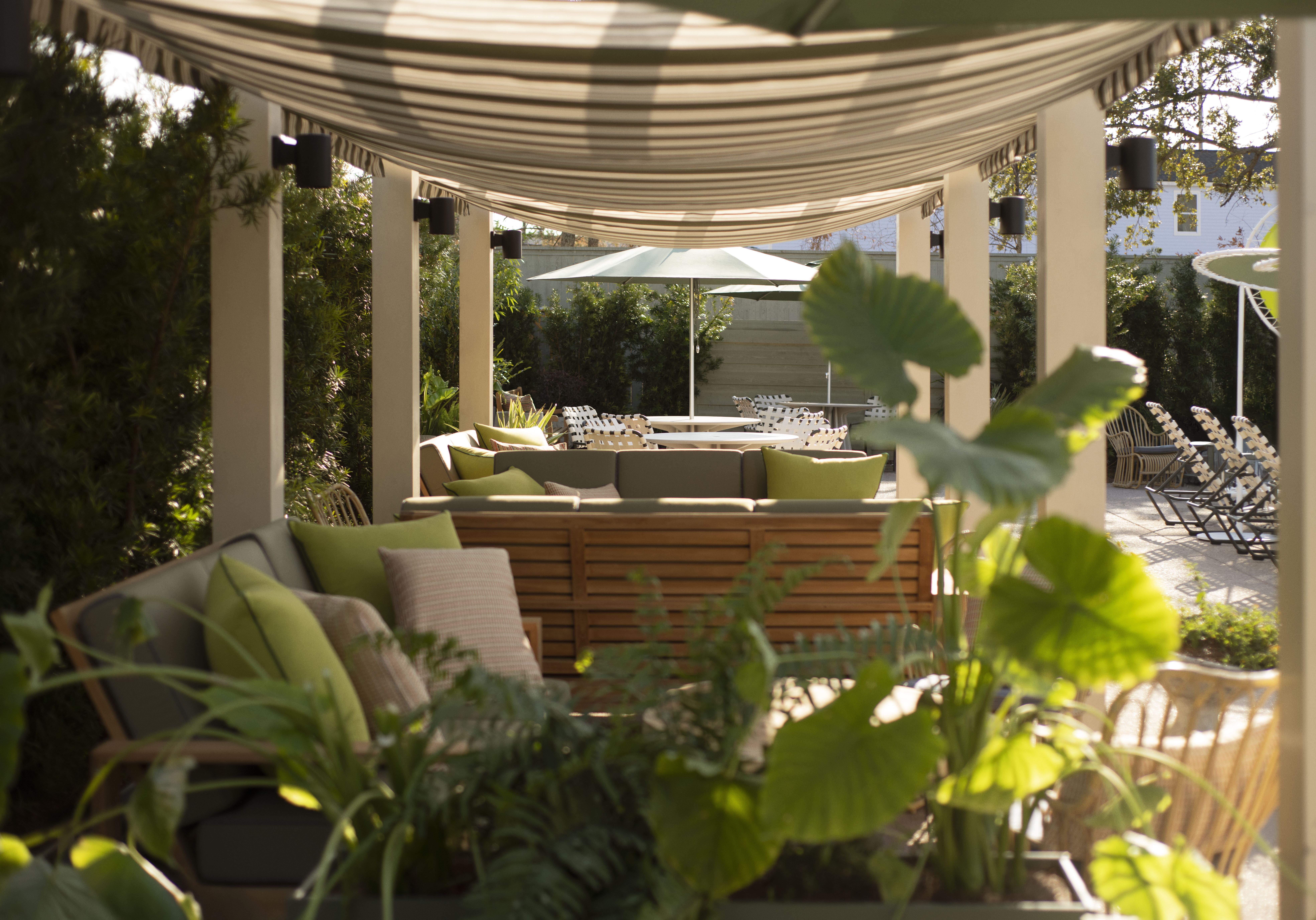 Pool cabanas are viewed cross-wise through columns as lush greenery surrounds the area.