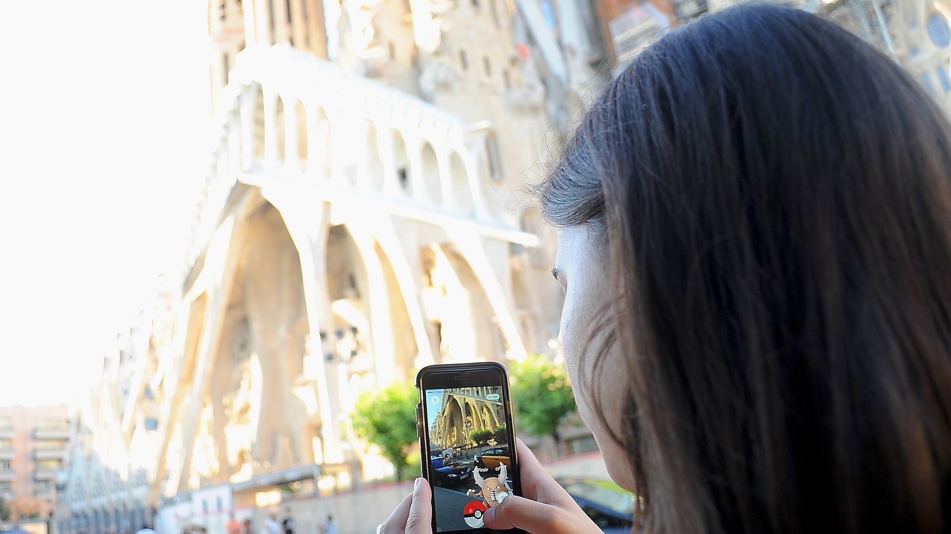 young woman plays Pokemon GO in front of Sagrada Familia, on July 15, 2016 in Barcelona