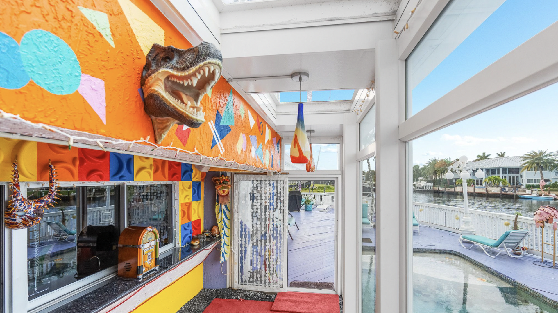 A taxidermied alligator head sticks out of an orange and multicolored wall beside a swimming pool. 