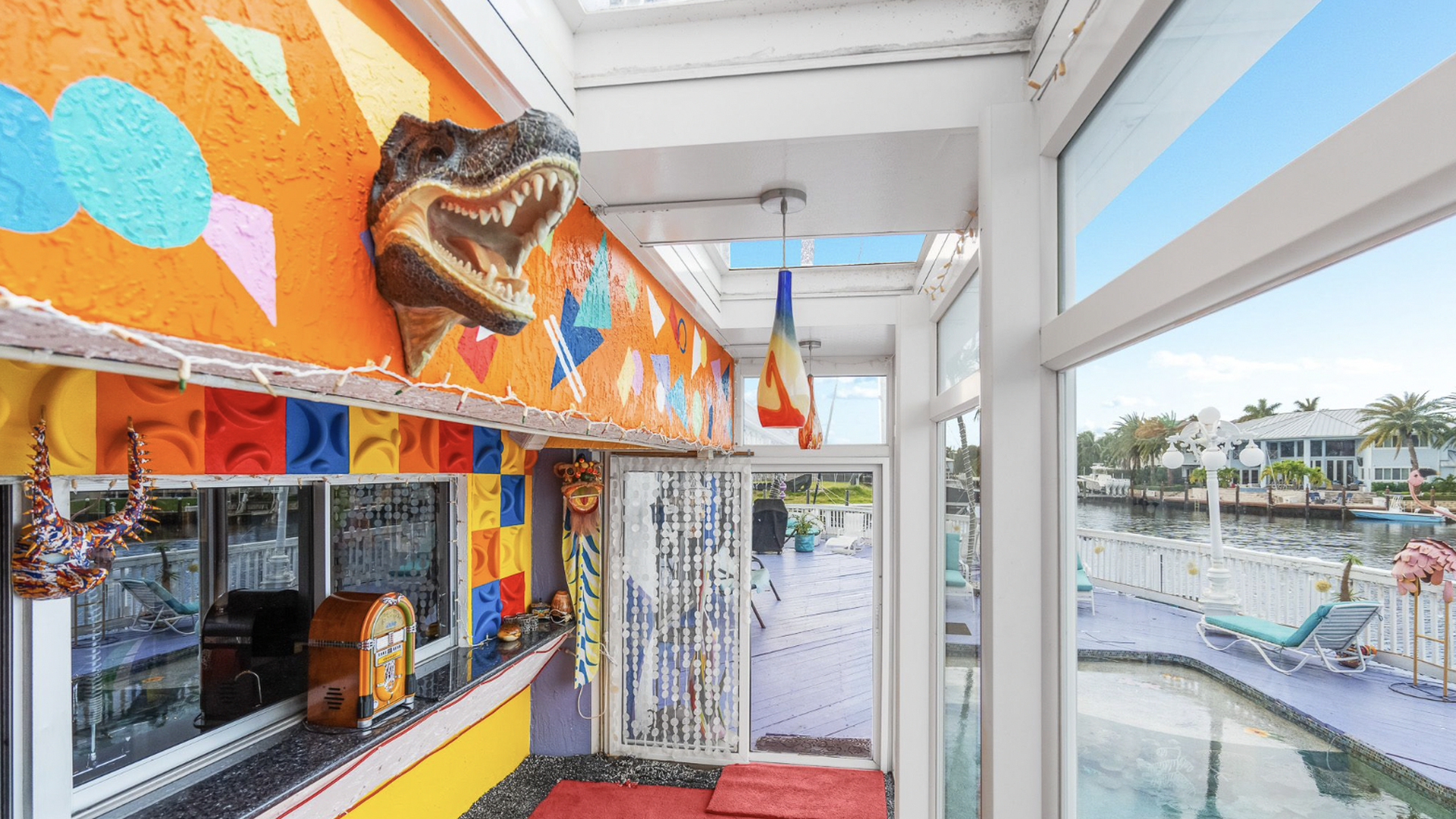 A taxidermied alligator head sticks out of an orange and multicolored wall beside a swimming pool.
