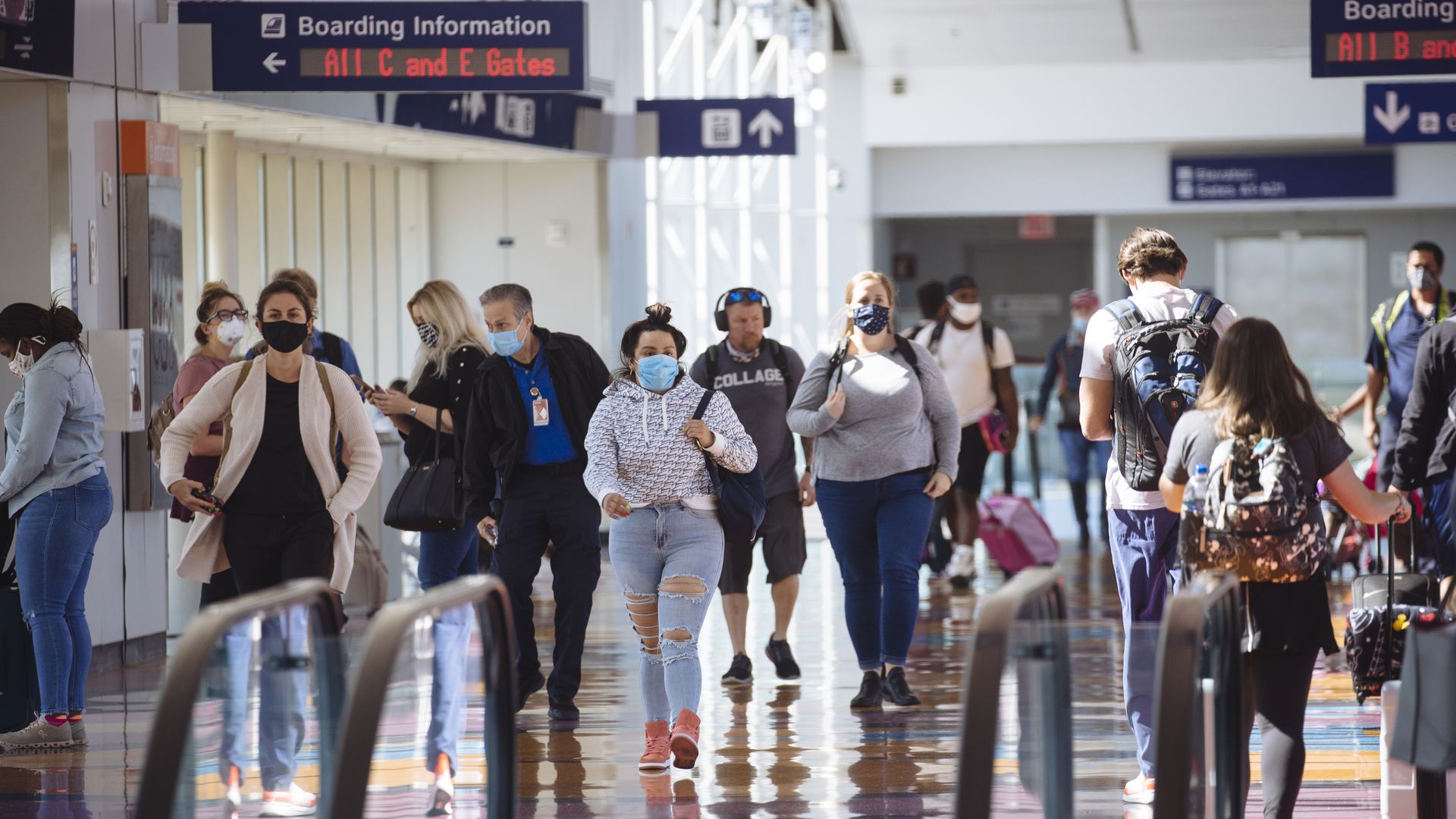 A crowd of masked people move through an airport terminal