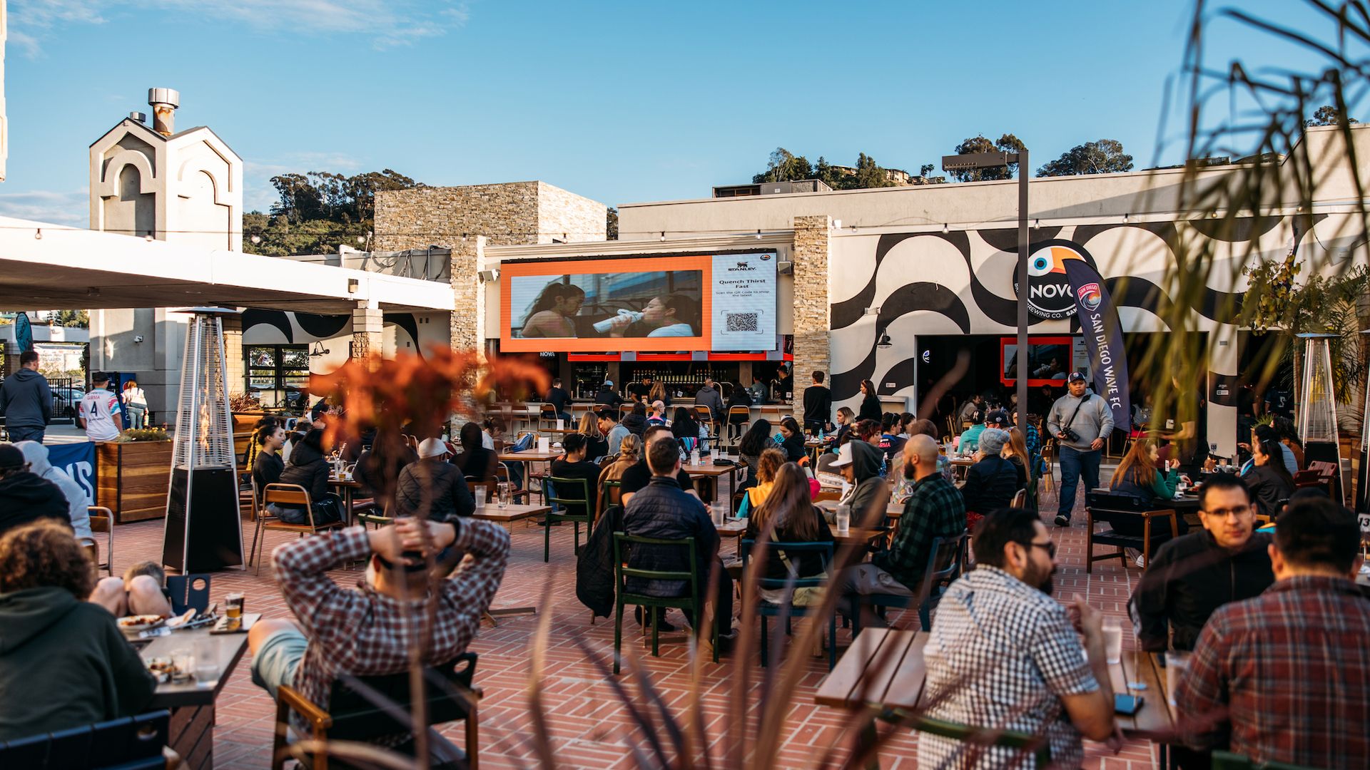 A patio full of soccer fans watching a game on a big screen. 