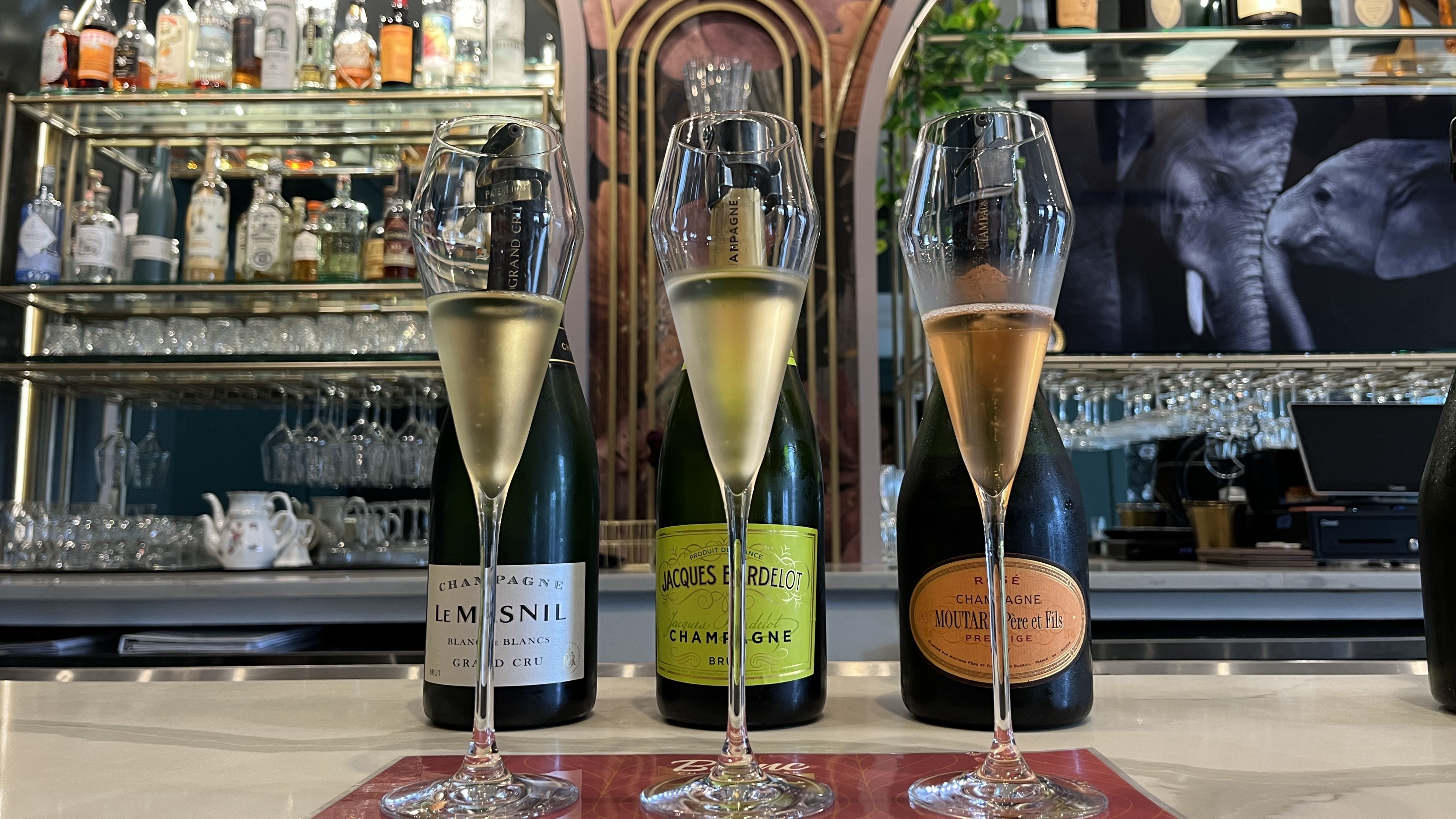 Three glasses of Champagne are lined up on a bar.