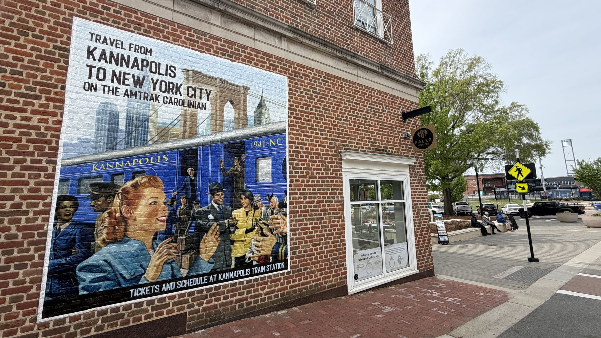 Brick wall mural showing travel from Kannapolis to New York City on the Amtrak Carolinian, with a blue train car and cheering people against a city skyline.