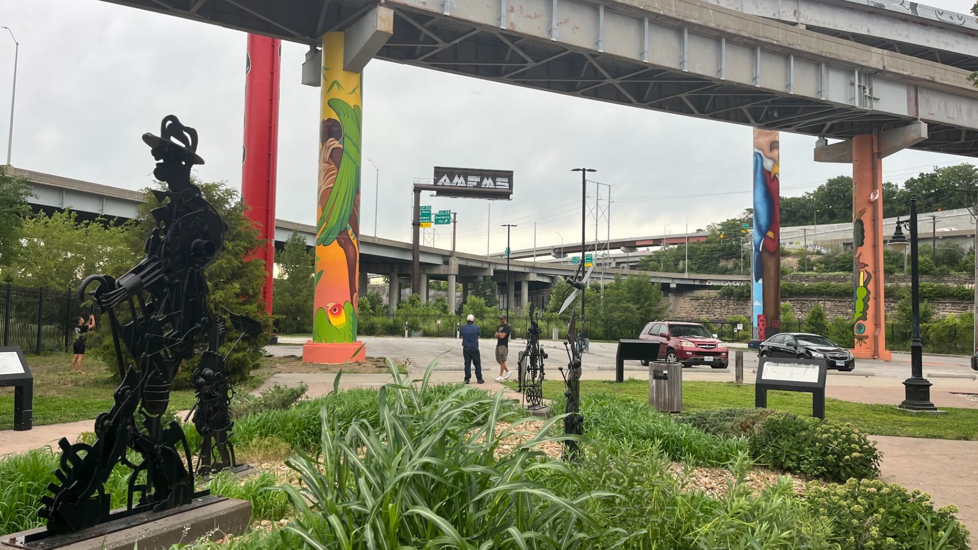 Photo shows four painted interstate pylons in Kansas City's West Bottoms near a metal statue depicting a slave.