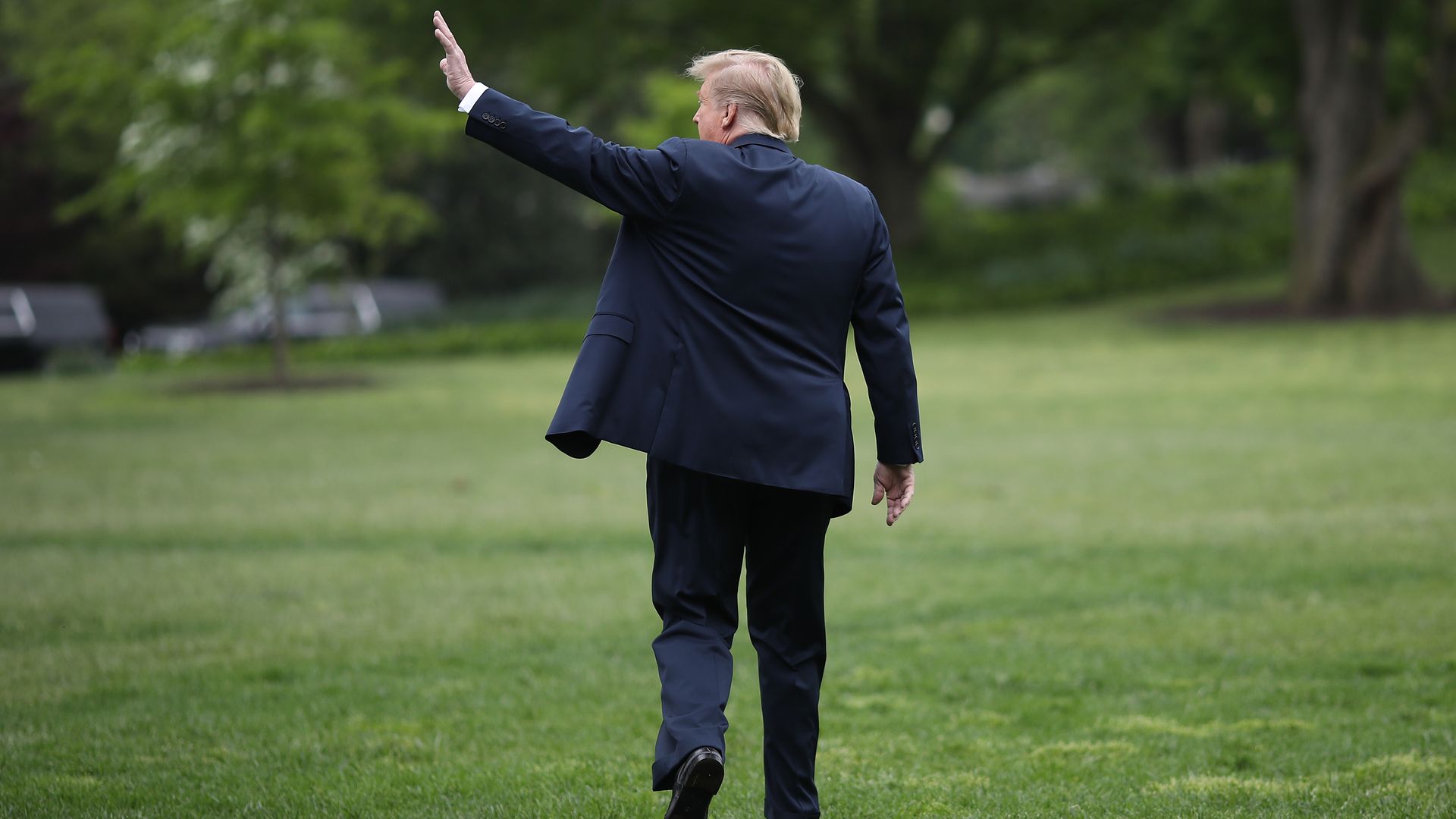 In this image, Trump walks away from the camera and waves, facing the left. 