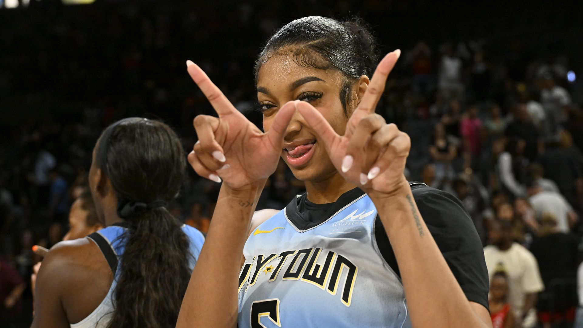 Photo of a basketball player in uniform flashing a "W" with her hands. 