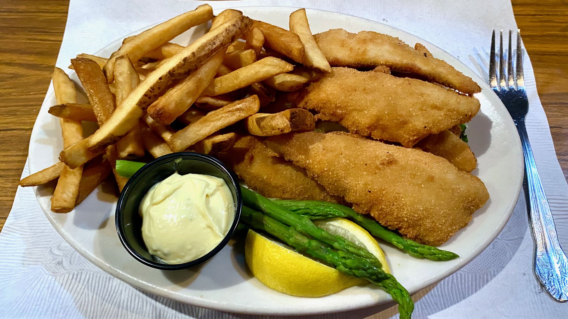 Perch. fries, asparagus, a lemon and tartar sauce on a plate on a wooden table
