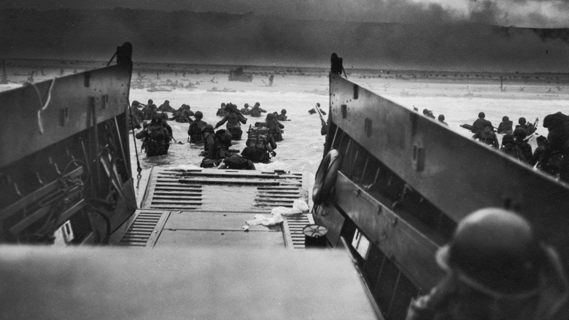 Black-and-white photo from inside a military aircraft as troops disembark onto a snow-covered airfield, rifles ready; dark cloudy sky and distant smoke on the horizon.
