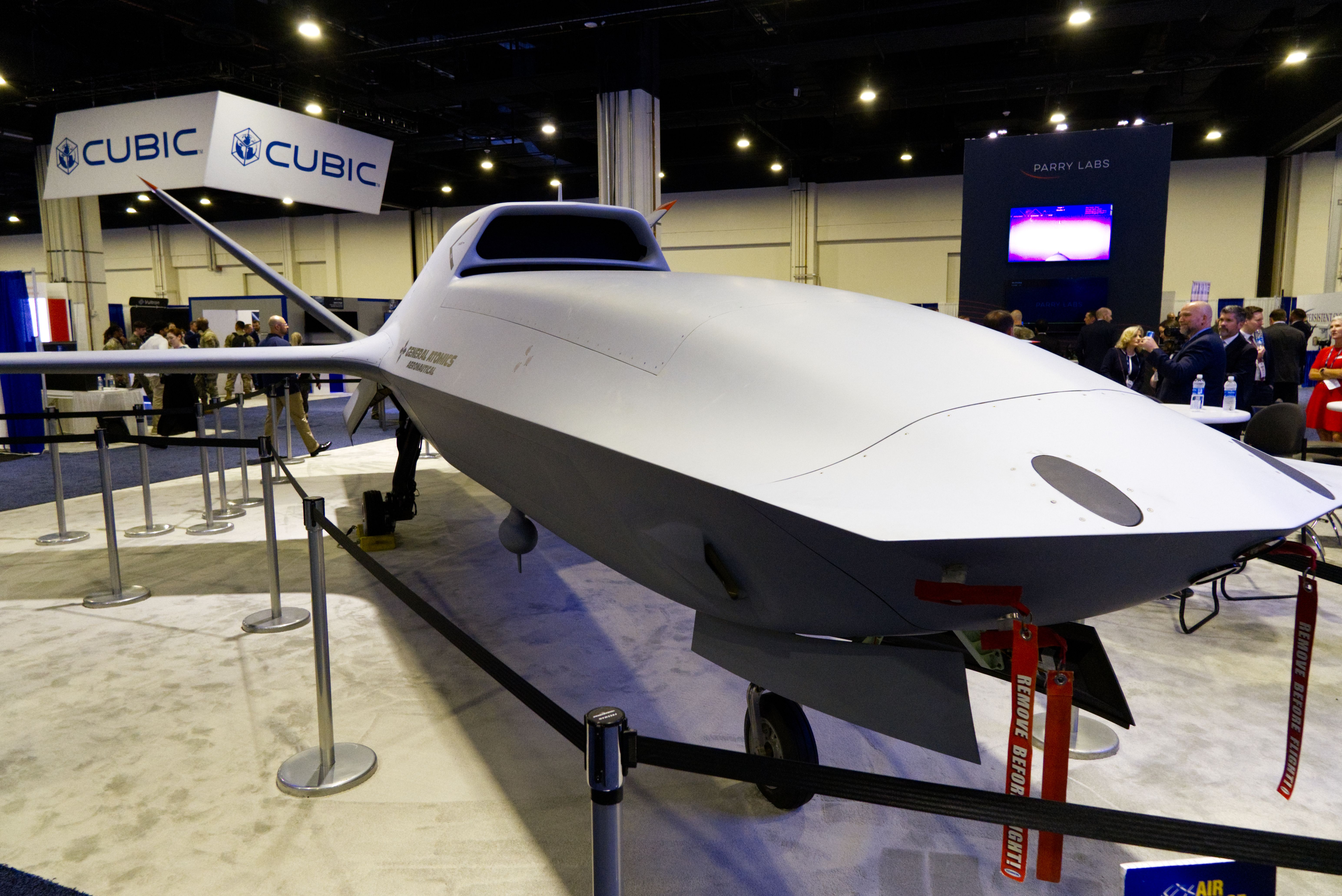 A large grey drone sits on a conference show floor. The carpet is off-white. A big sign in the back reads CUBIC.