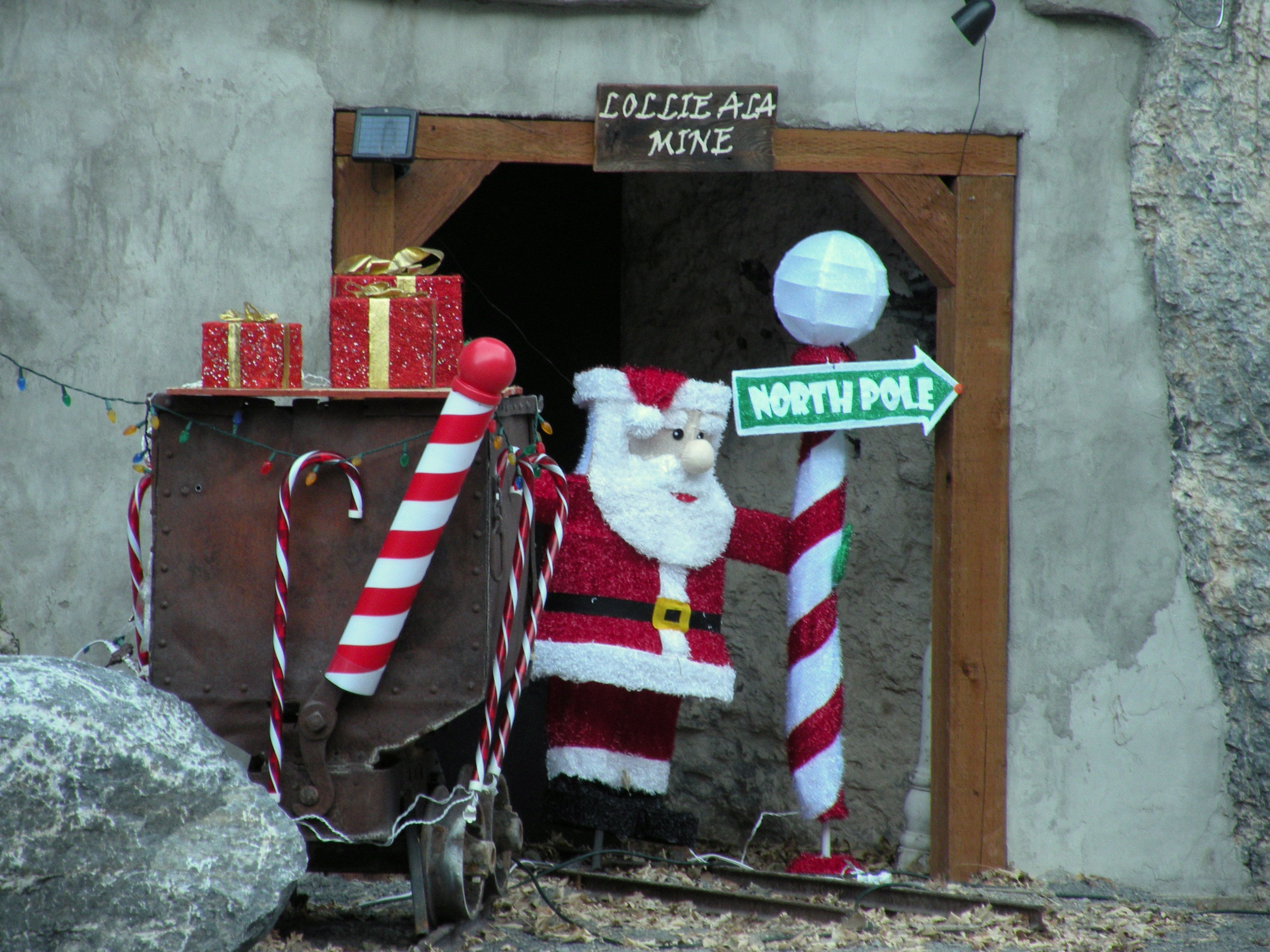A mine entrance is guarded by a Santa statue with gifts, candy canes and a red and white signpost with an arrow labeled "North Pole"