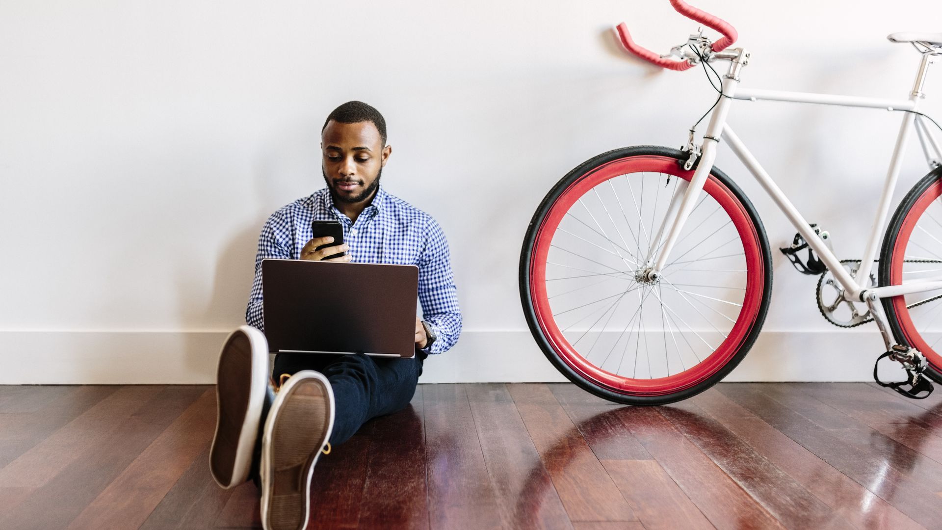 Man with cellphone and laptop leans against wall with bicycle