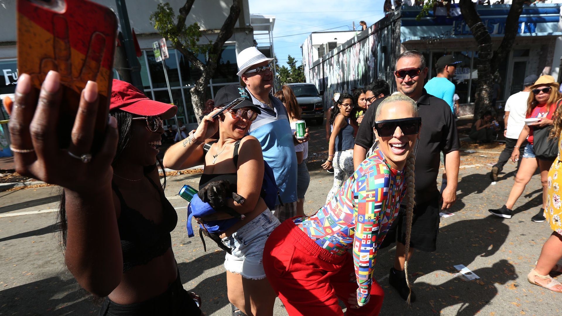 A woman wearing red pants, a colorful long-sleeved shirt and black sunglasses dances in the street.