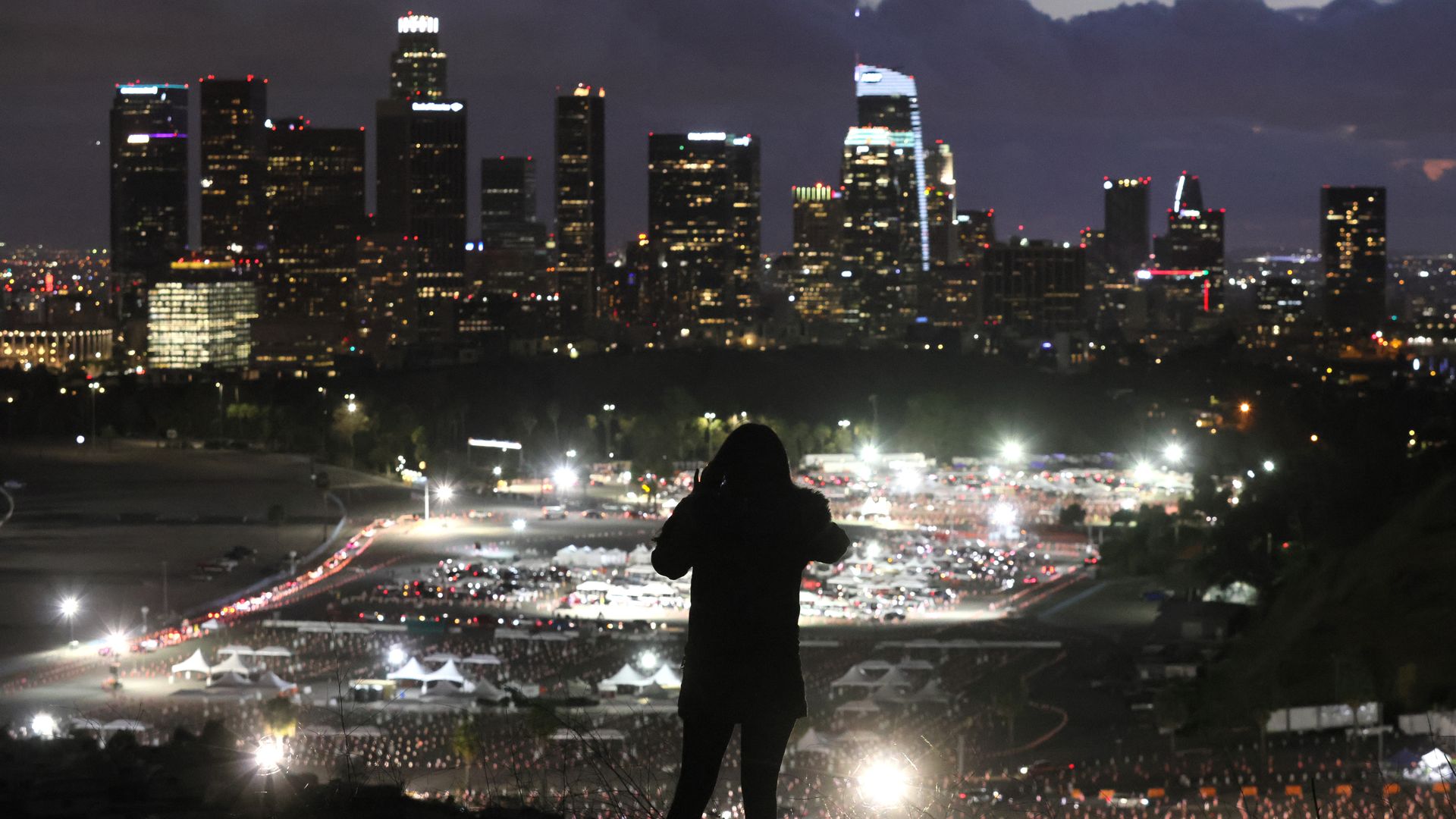 Silhouette of someone in a winter jacket standing in front of a lighted stadium