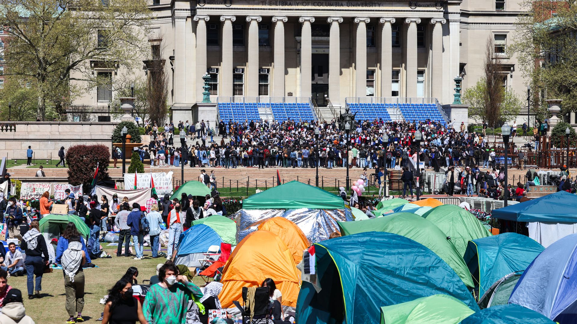 About seven tents are seen on Columbia's lawn with people walking in the foreground and background of the image.