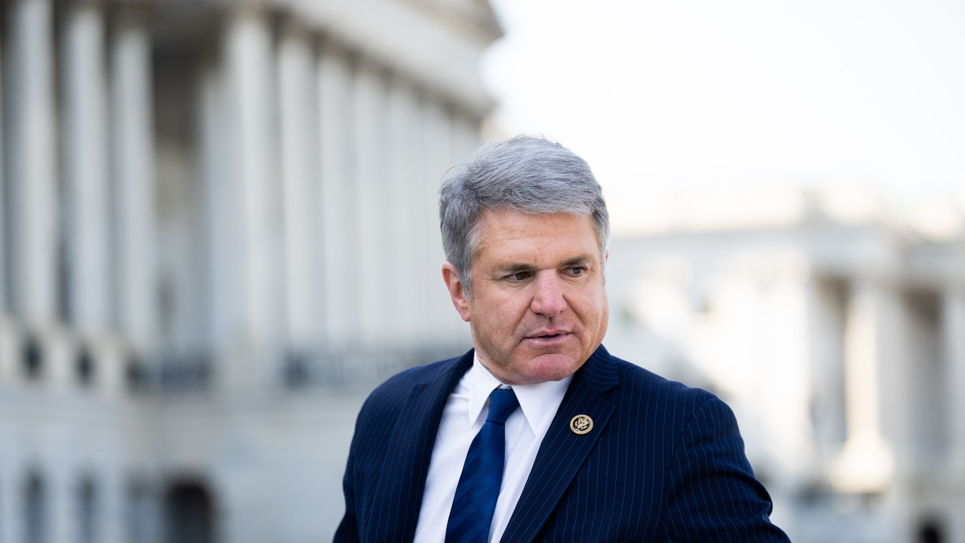 Rep. Michael McCaul, wearing a blue pinstripe suit, white shirt and blue tie, stands in front of the Capitol.
