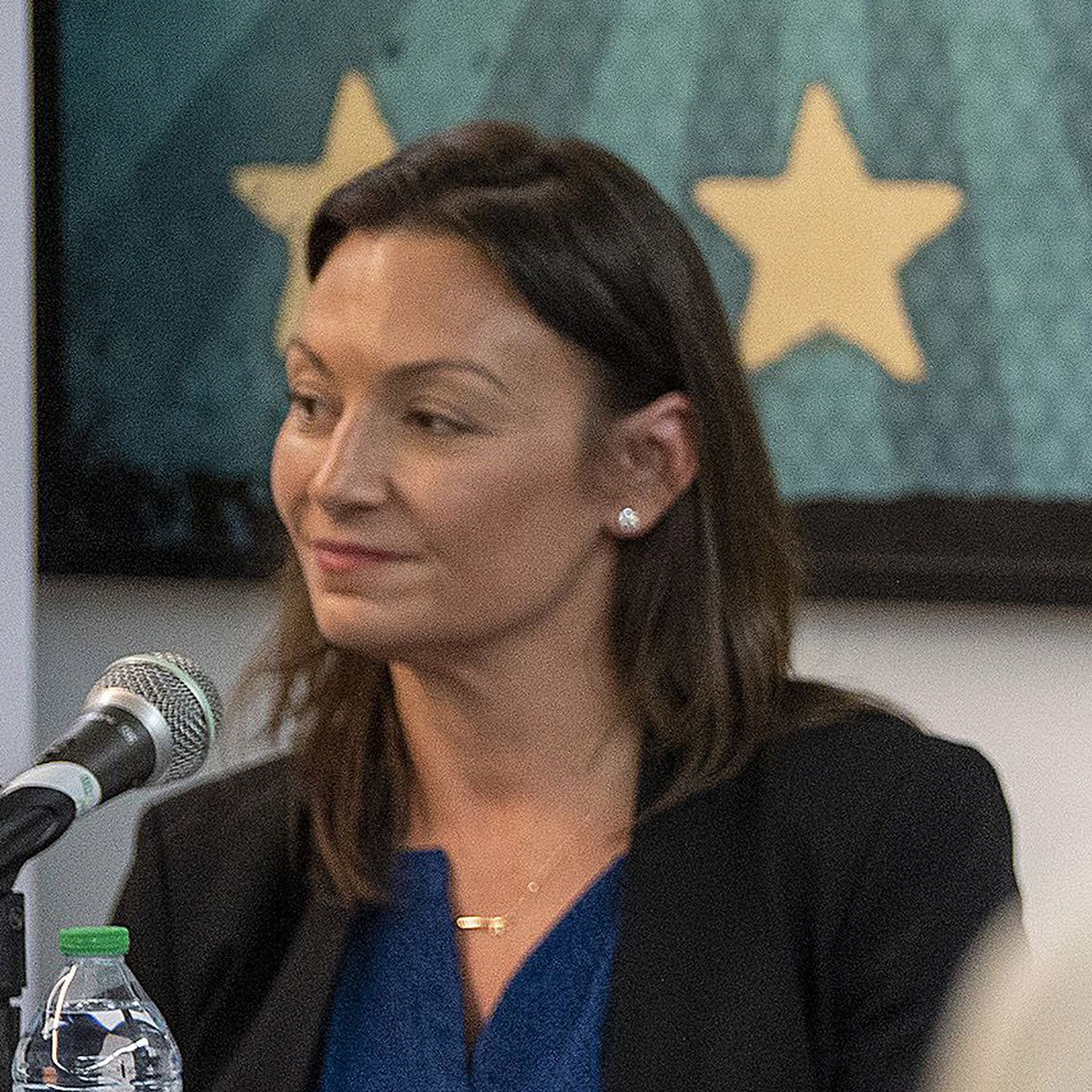 Florida Agriculture Commissioner Nikki Fried smiles as she sits behind a microphone. 