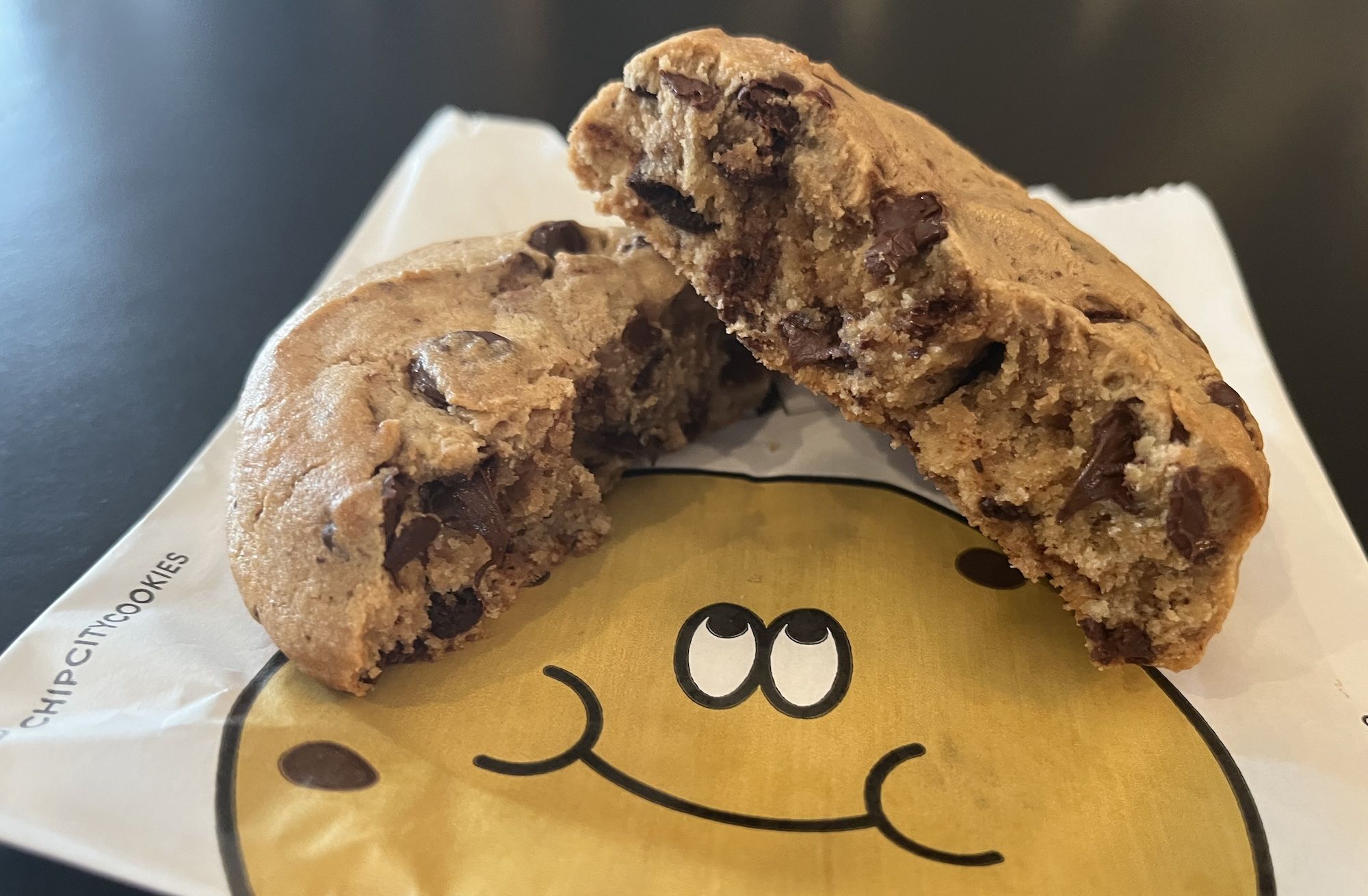 Chocolate cookie cut in half with both sides on top of bad with drawing of a smiling cookie.