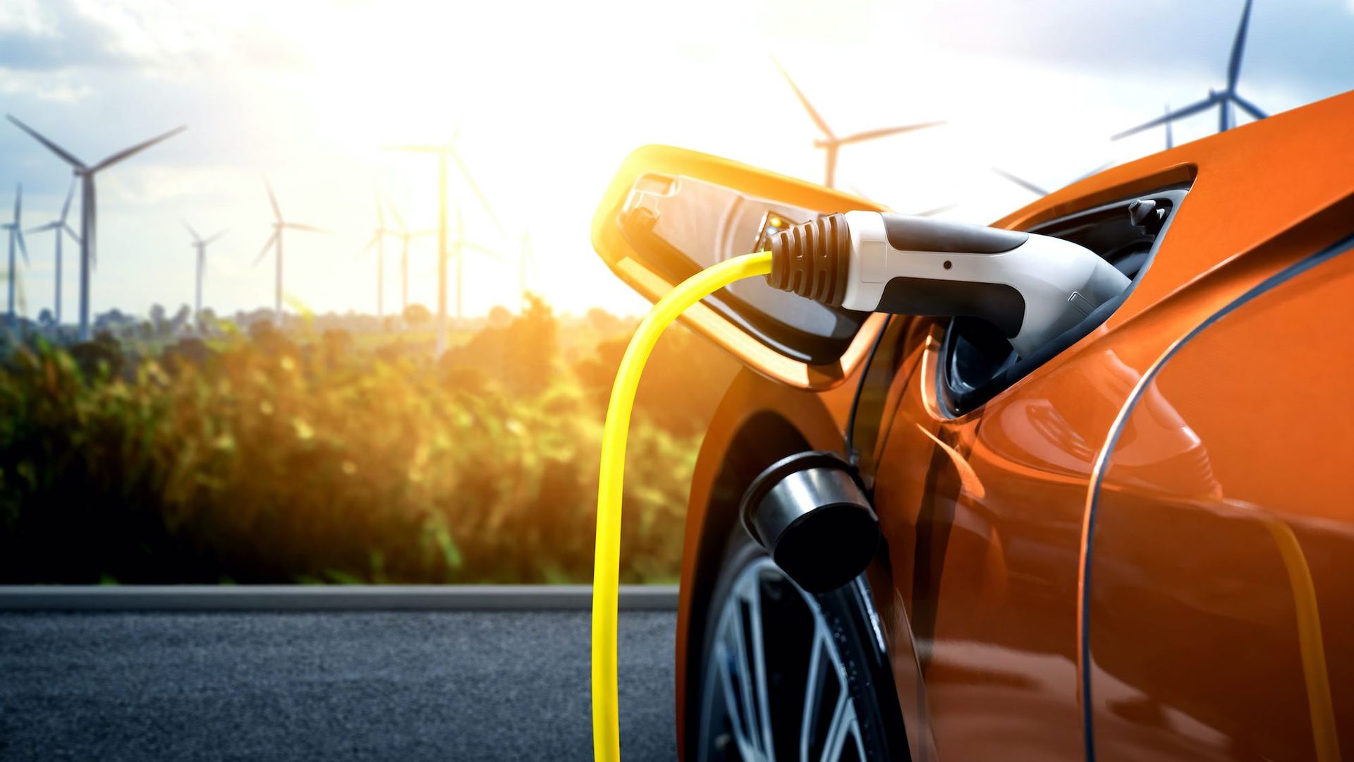 An orange car is plugged into an electric charger