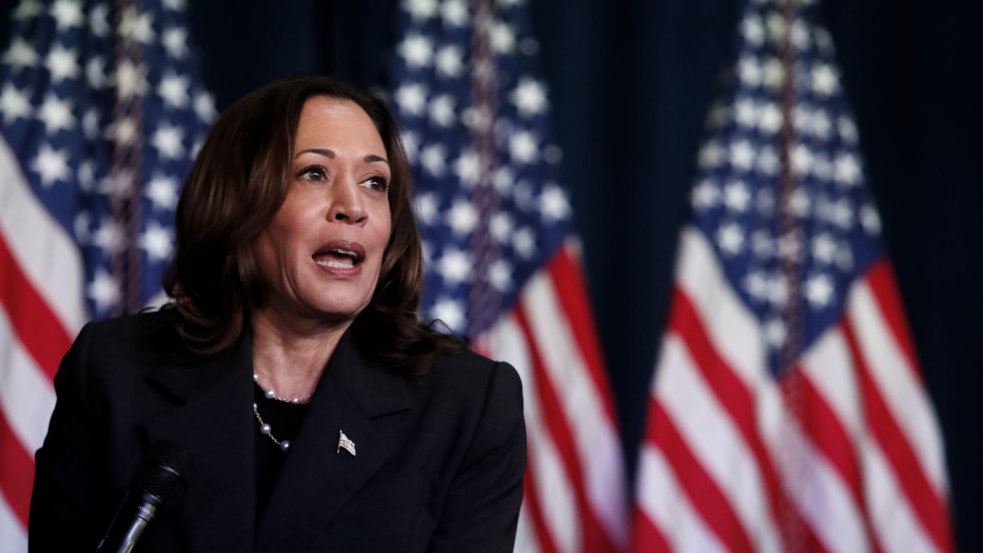 Kamala Harris in front of three U.S. flags