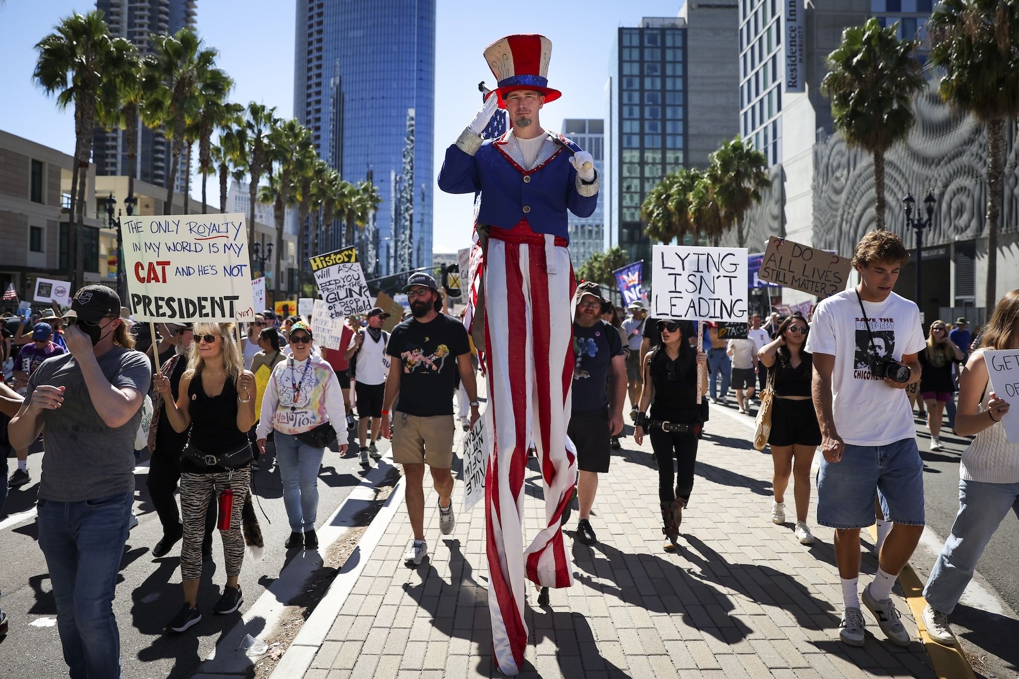 A man on stilts dressed as Uncle Sam salutes as he marches with others along the palm tree-lined Pacific Highway during a "No Kings" protest in downtown San Diego.