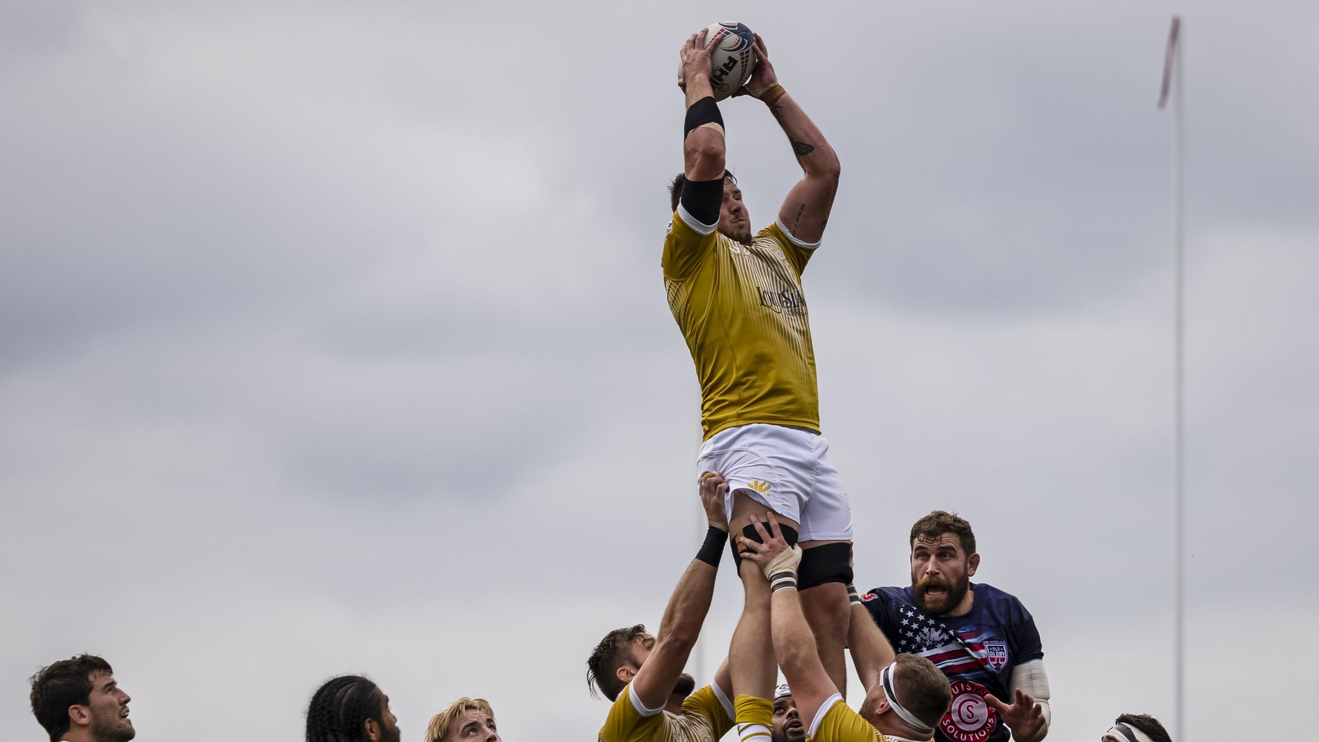 Nikola Bursic hoists a rugby ball in the air as his teammates hold him aloft above them.