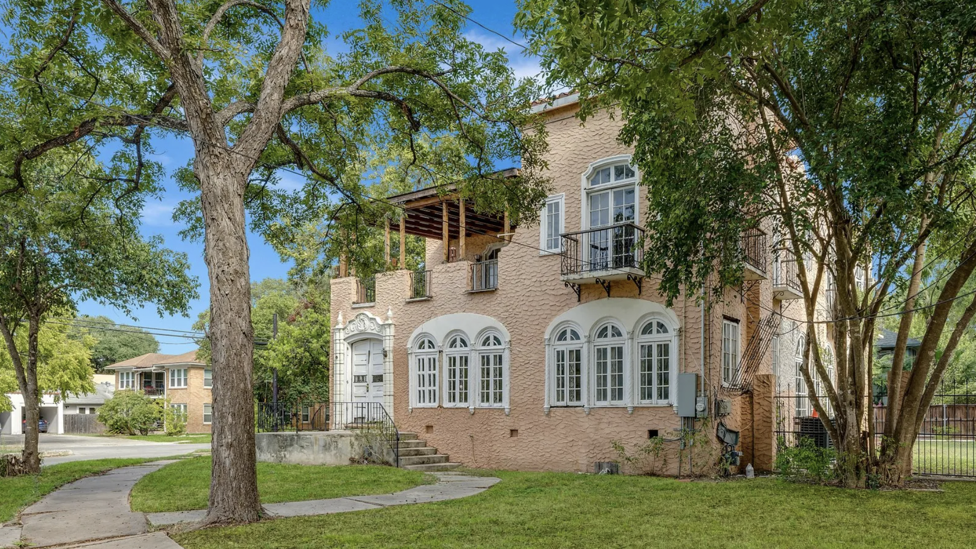 A historic pink home nestled behind tall trees.