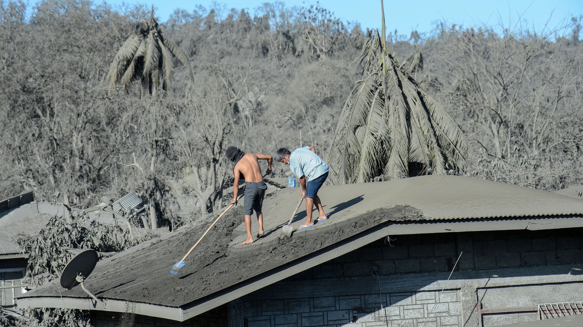   Residents clean the roof of their home covered in mud and ash from the nearby Taal volcano. 