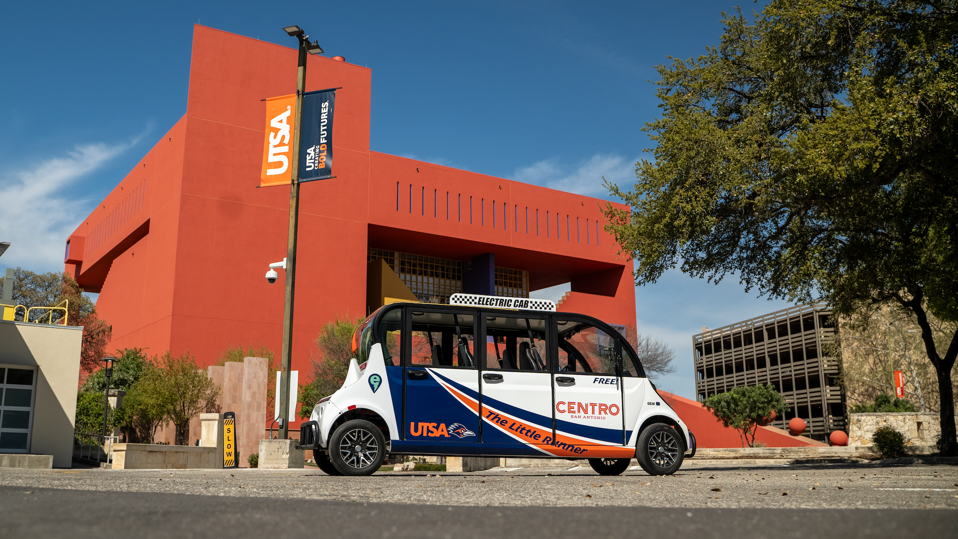 A blue, orange and while go kart-like shuttle is parked in front of the burnt orange Central Library.