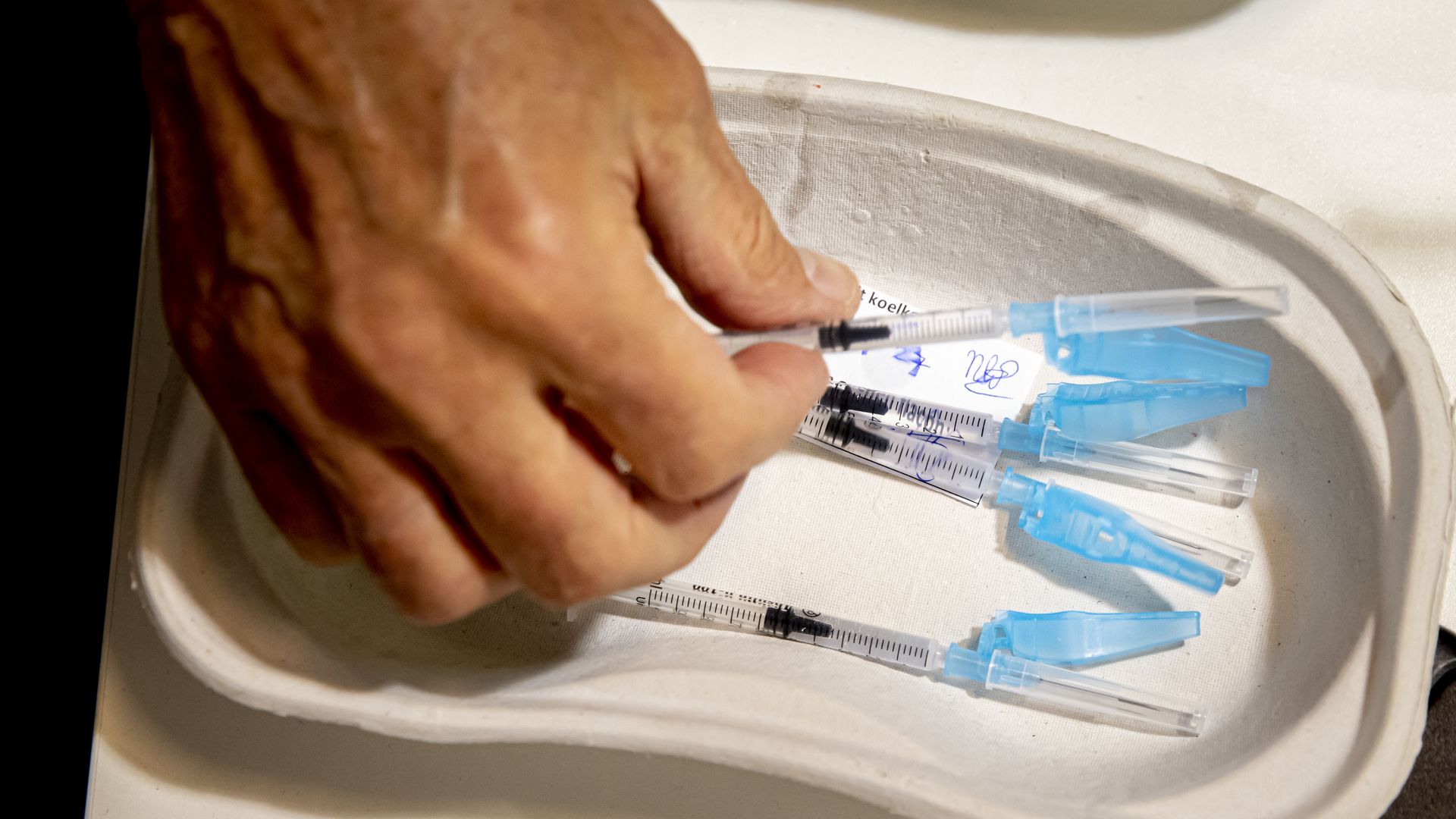 Photo of a hand picking up a vaccine shot from a container