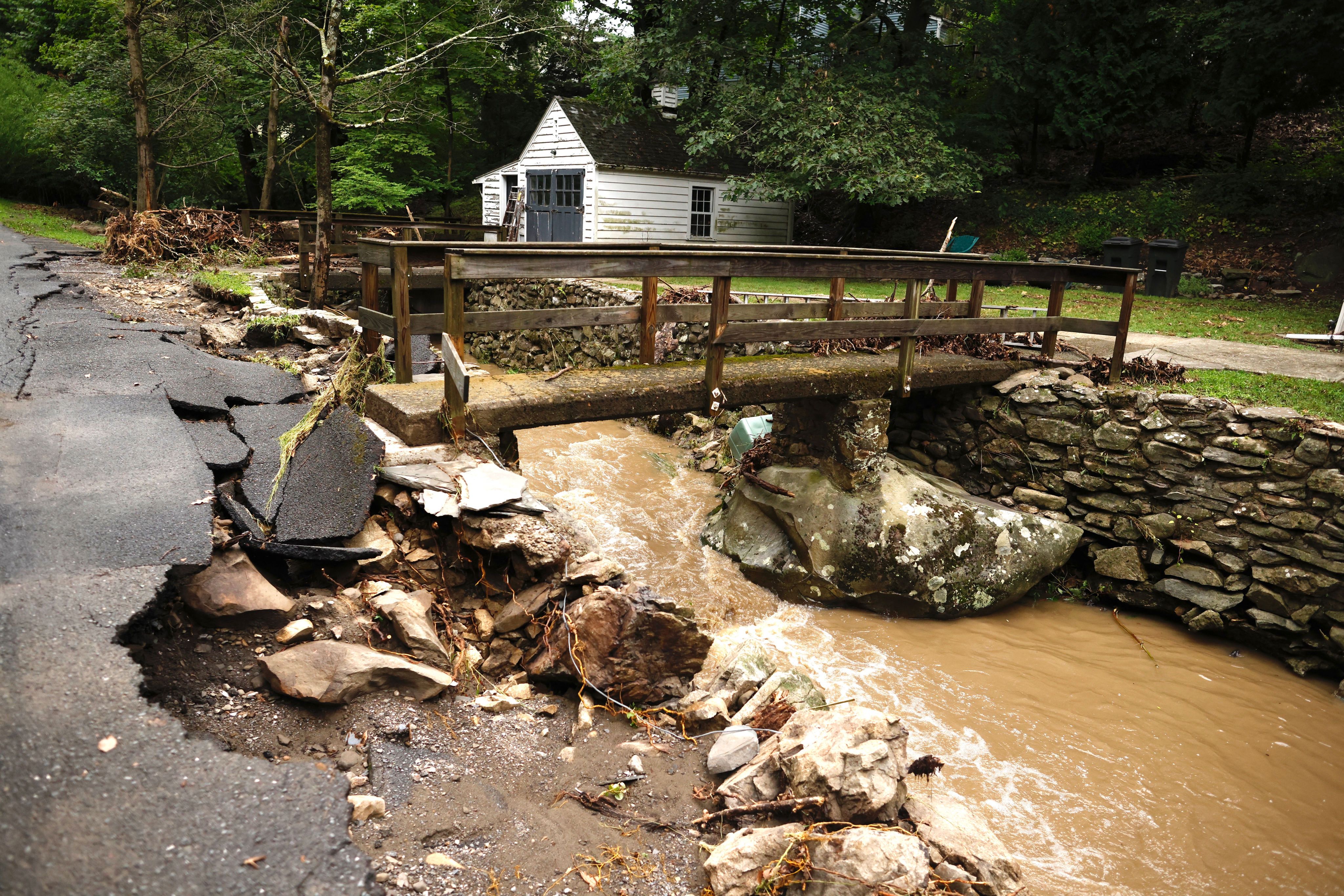 A road is damaged as water in a creek rushes after heavy rainfall in Cornwall-On-Hudson, New York, on July 10, 2023. 