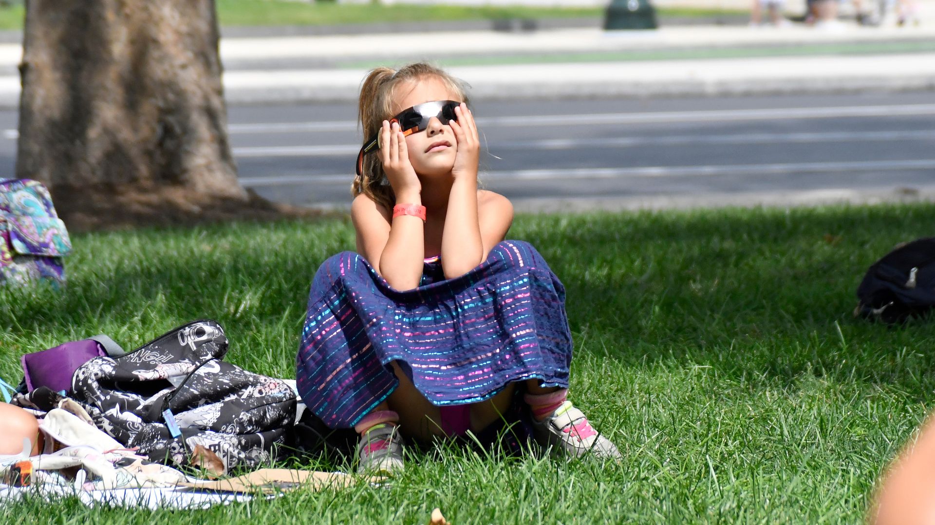 A girl sits on a lawn and watches an eclipse. 