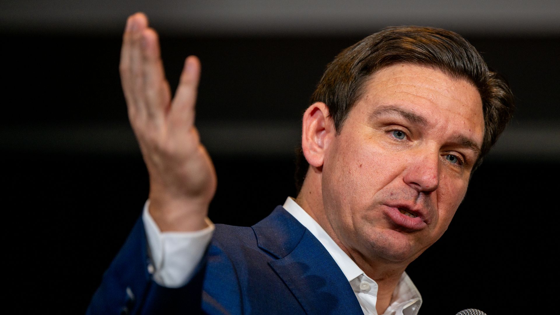 Ron DeSantis speaks into a microphone and gestures with his right hand.
