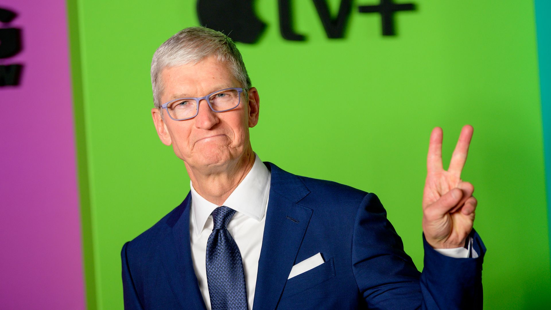Apple CEO Tim Cook in a suit and tie, flashing a peace sign