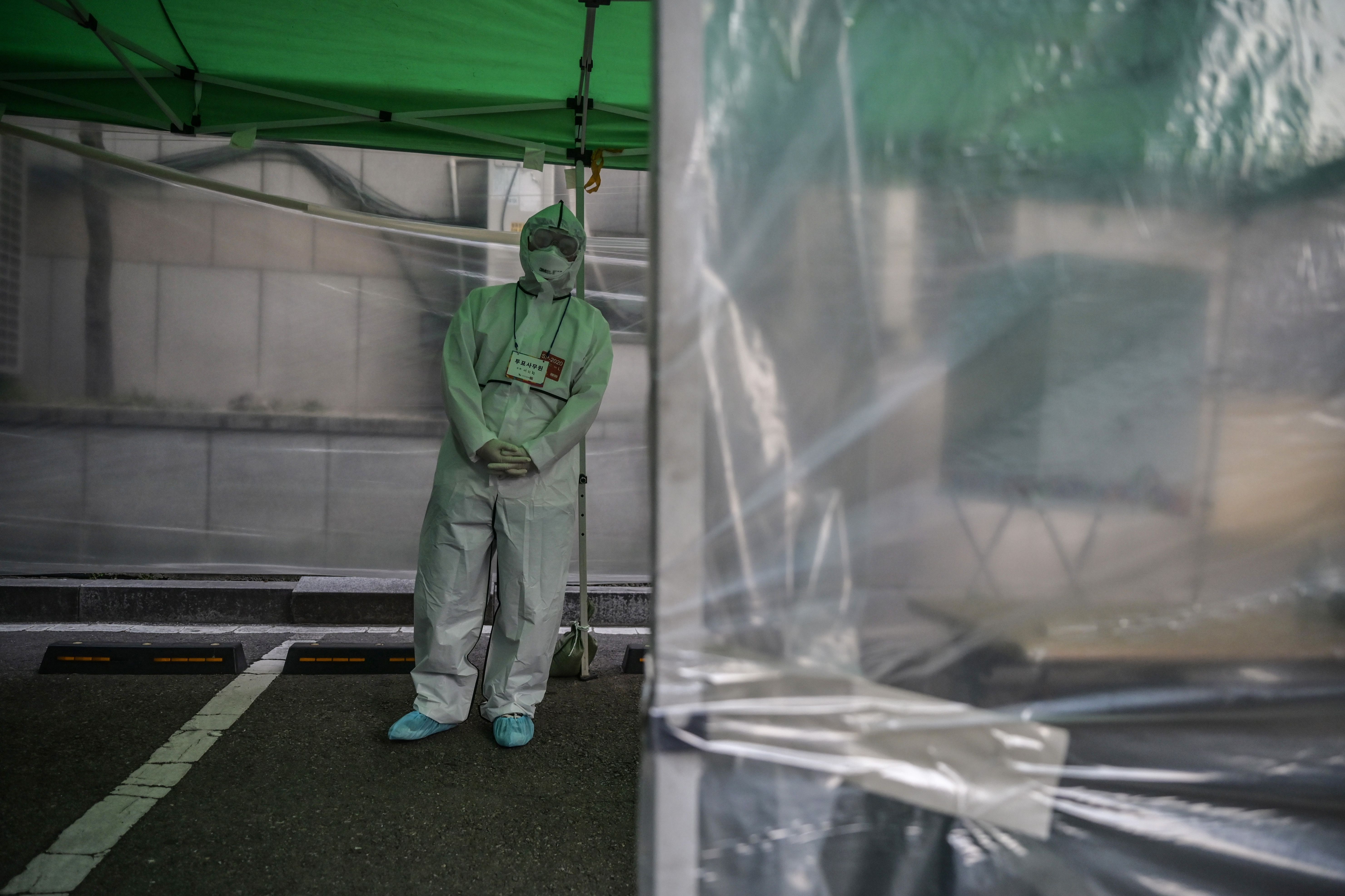 In this image, a man in hazmat gear stands in a clear plastic tent