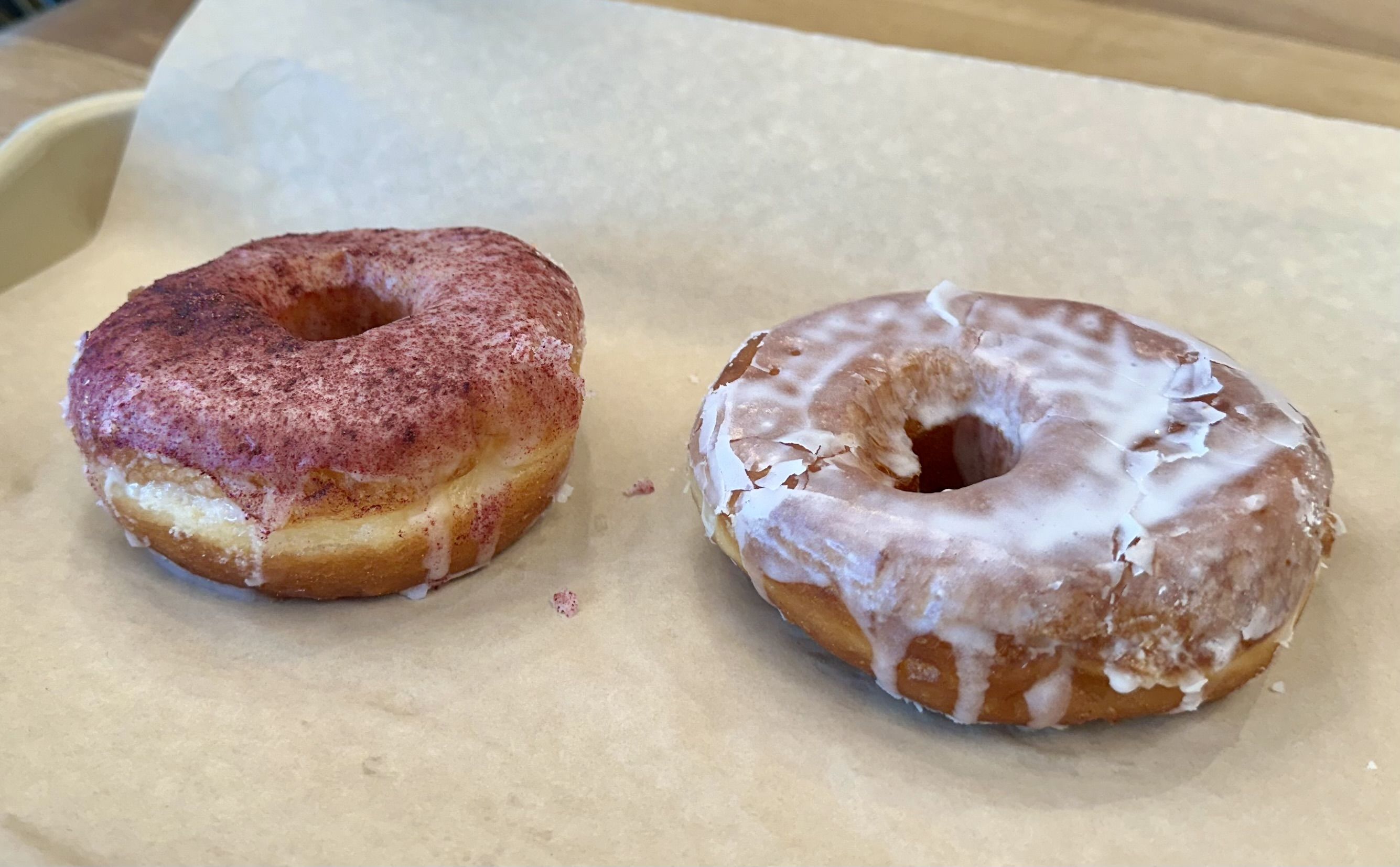 A blackberry chevre and glazed doughnut sitting on paper on a metal tray.