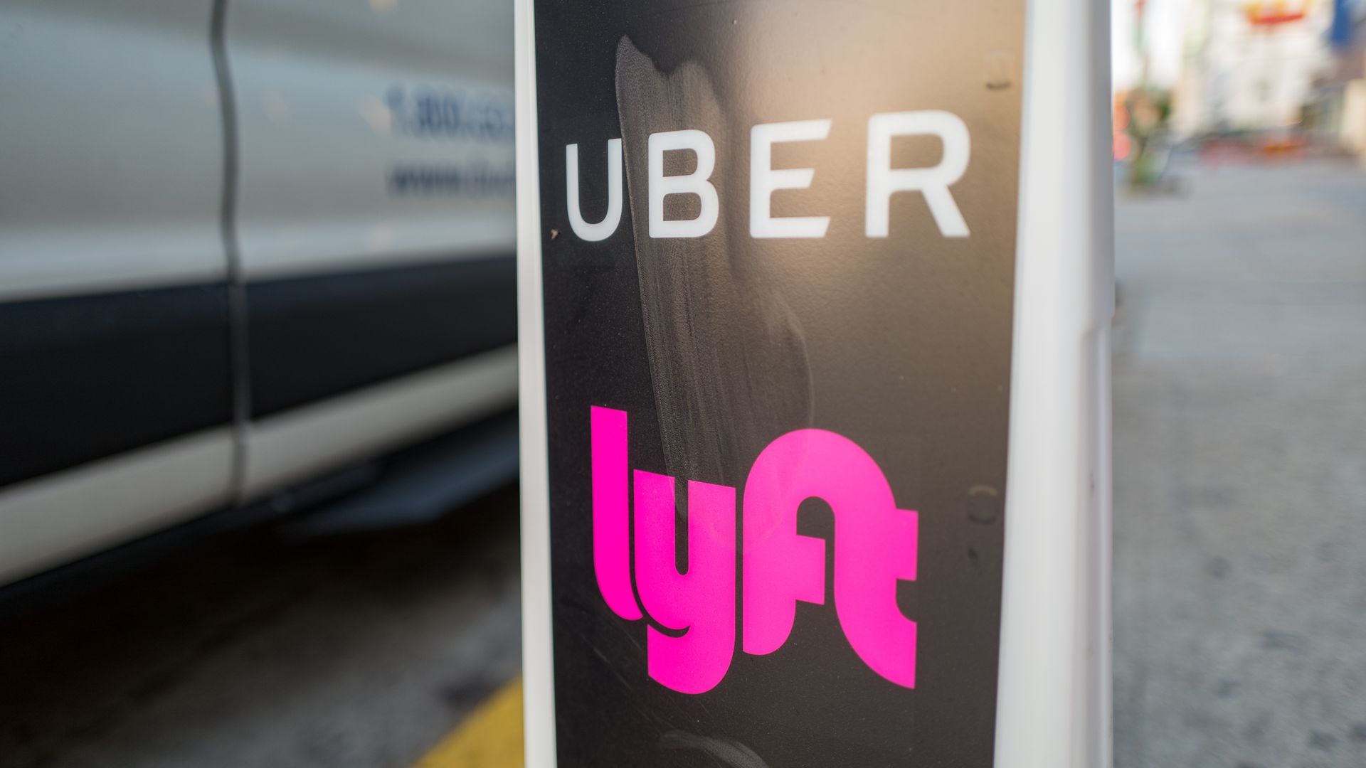 In this image, the Uber and Lyft logos are stacked on top of one another on a pole