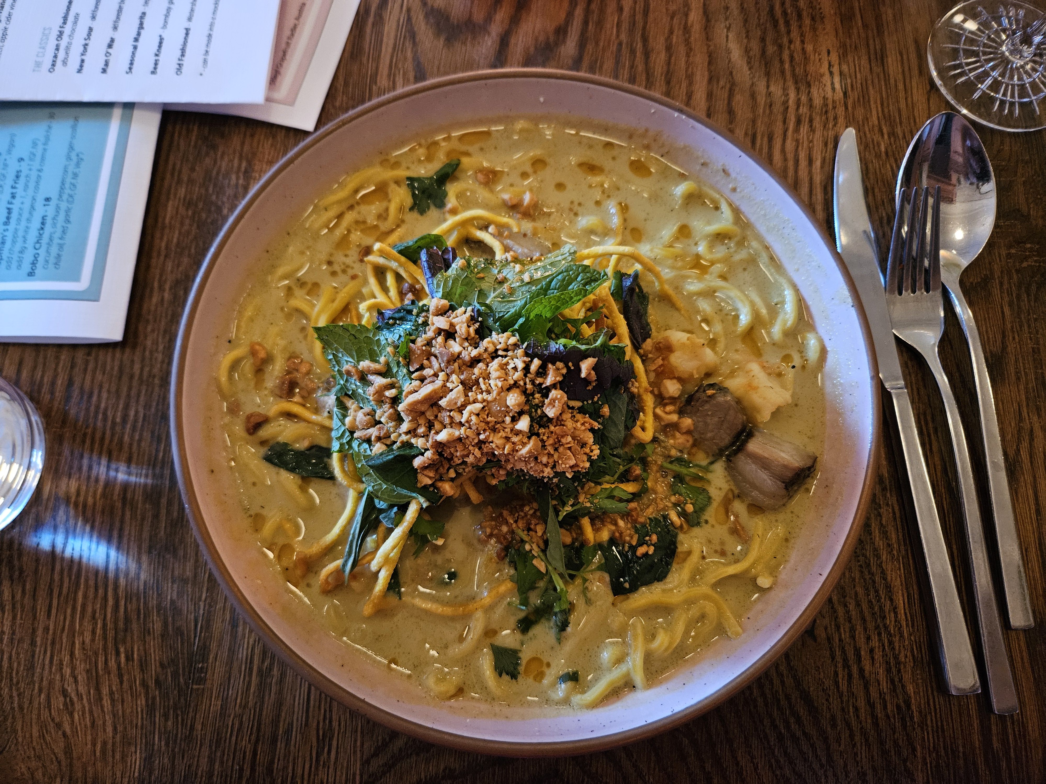 An overview of a khao soi dish with pork and shrimp, noddles and a yellow broth topped with peanuts