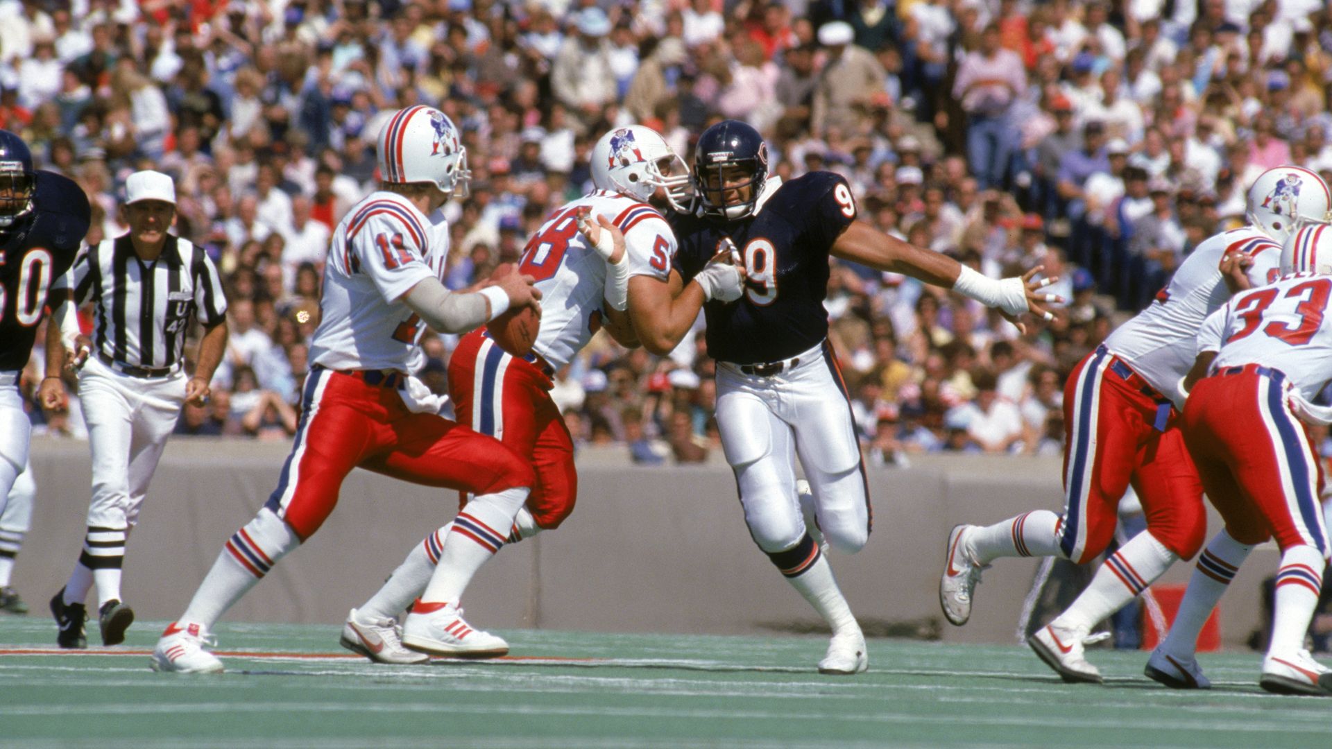 Football players play football on a field in front of fans. 